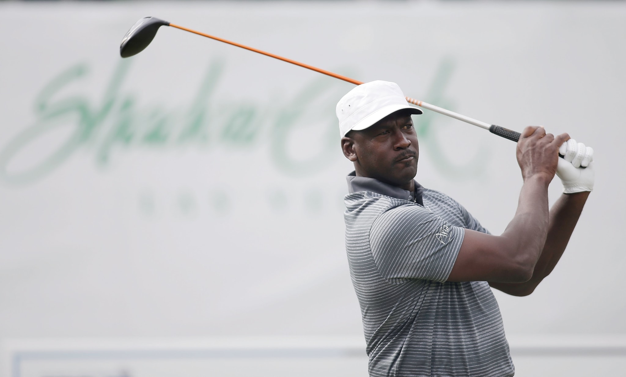 Golfer mid-swing at a tee box with sponsor logos in background