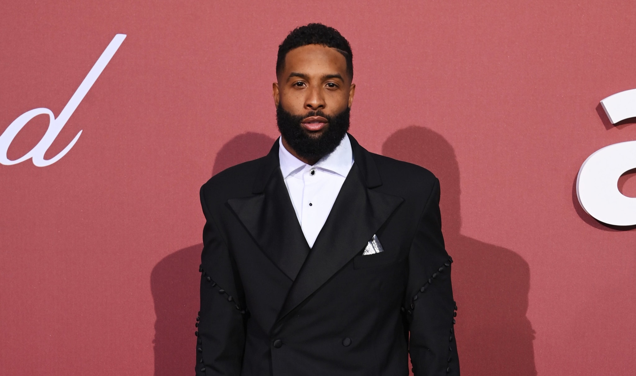 Odell Beckham Jr. on the red carpet at the amfAR event, wearing a black tuxedo with a white dress shirt and black bow tie