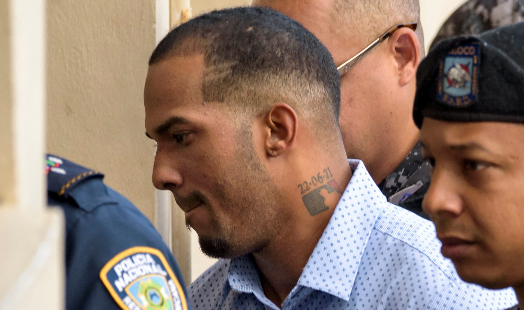 Yankees' pitcher Domingo Germán in a white shirt escorted by police officers, including one in a police beret