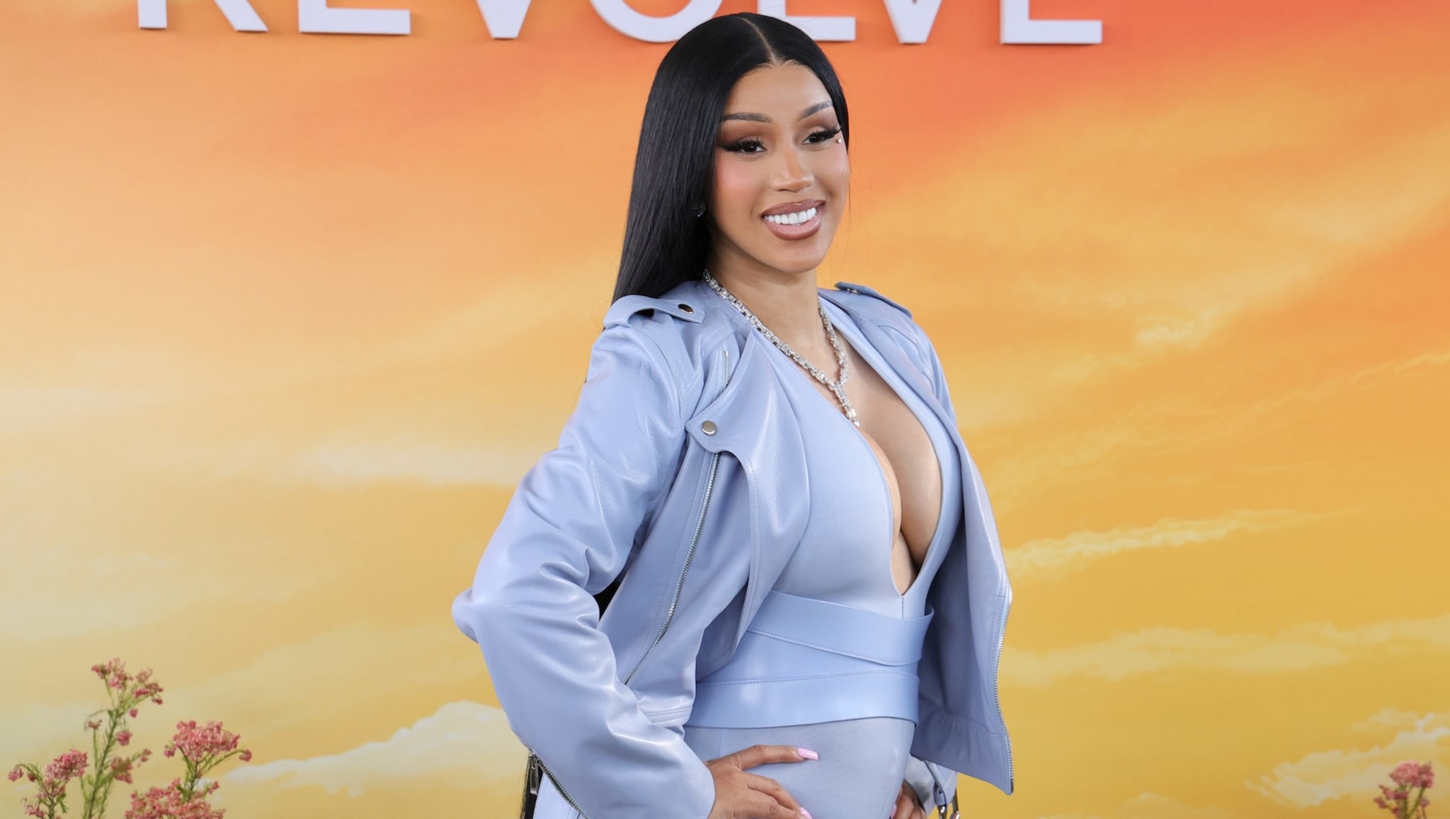 Cardi B at the Revolve festival, posing for a picture wjhile wearing a light blue jacket and dress.