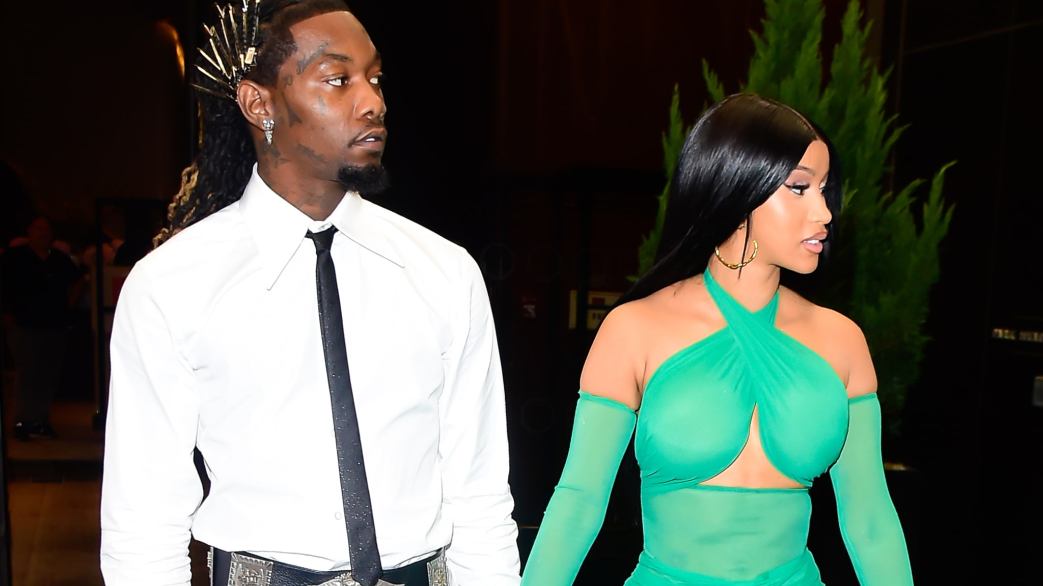 Offset and Cardi B walking together, Offset wearing a white shirt and black pants, Cardi B in a stylish, sheer green dress