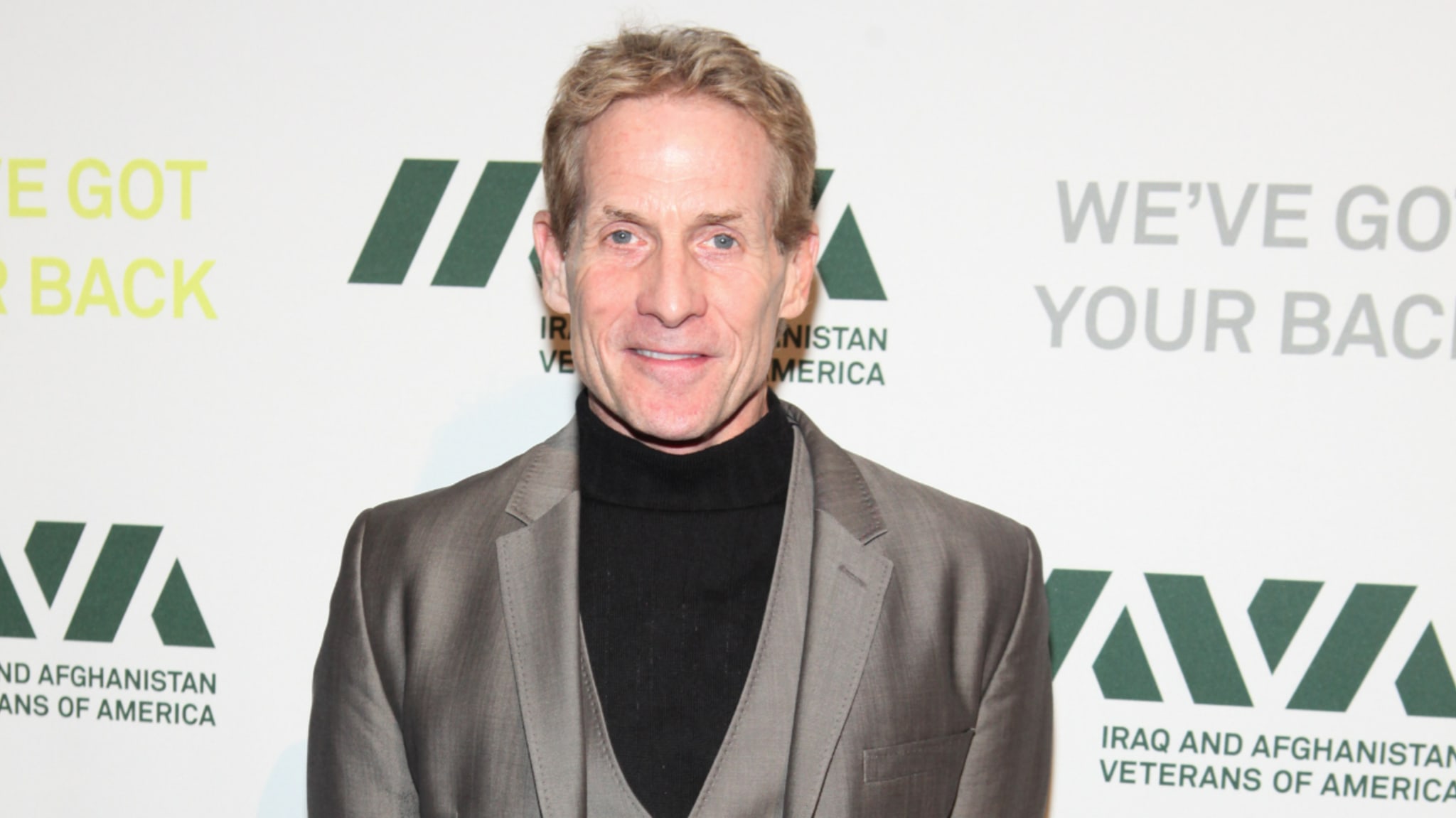 Skip Bayless, wearing a sleek suit and turtleneck, attends an event