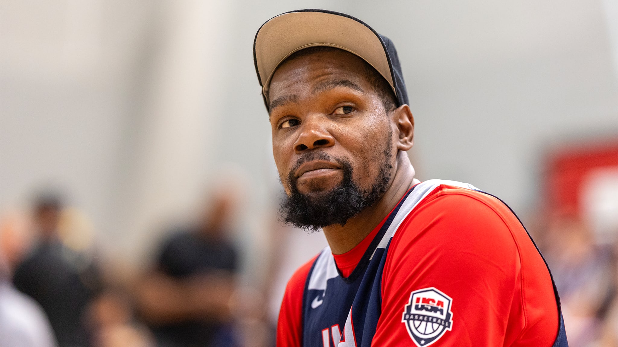 Kevin Durant, wearing a USA Basketball jersey and cap, looks to the side while attending an event