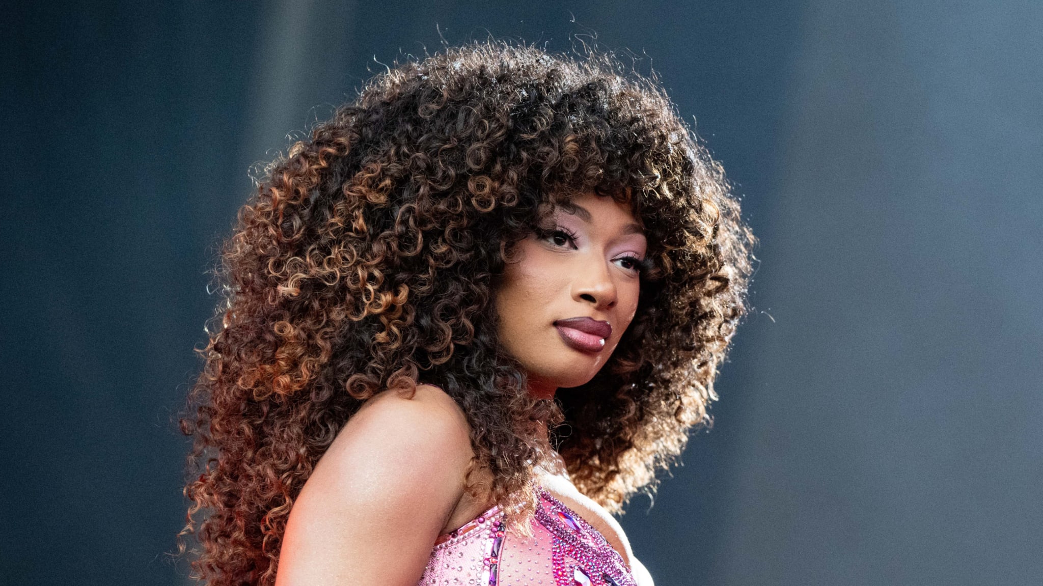 Megan Thee Stallion with voluminous curly hair, wearing a sparkly sequined outfit, looking back over her shoulder