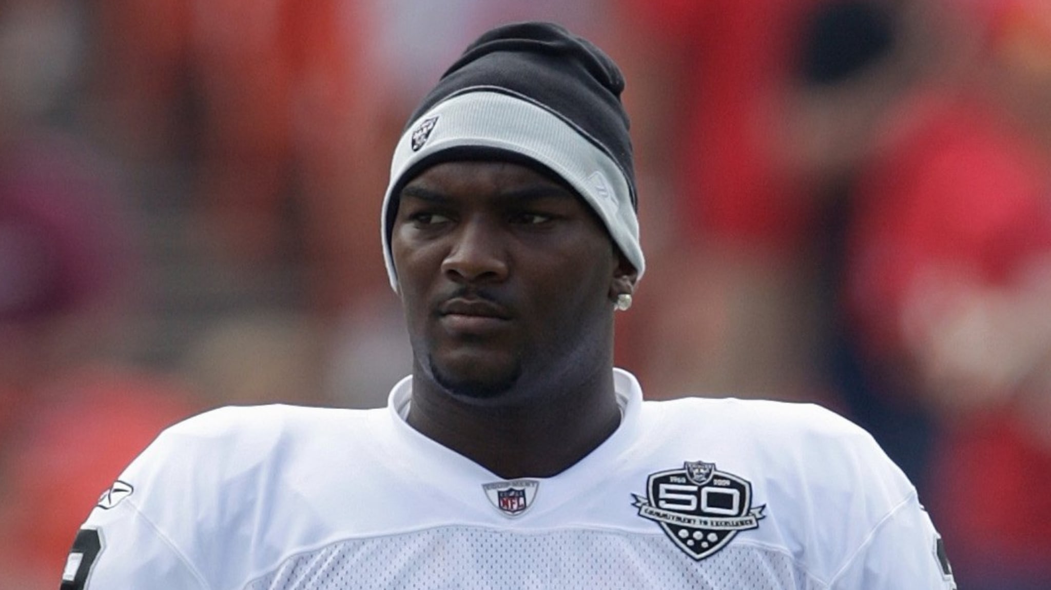 A football player, wearing a white jersey with a "60" emblem and a black and grey beanie, looks serious