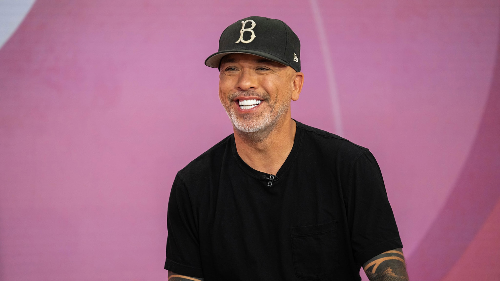 A man is smiling and wearing a dark cap with a "B" on it and a dark T-shirt
