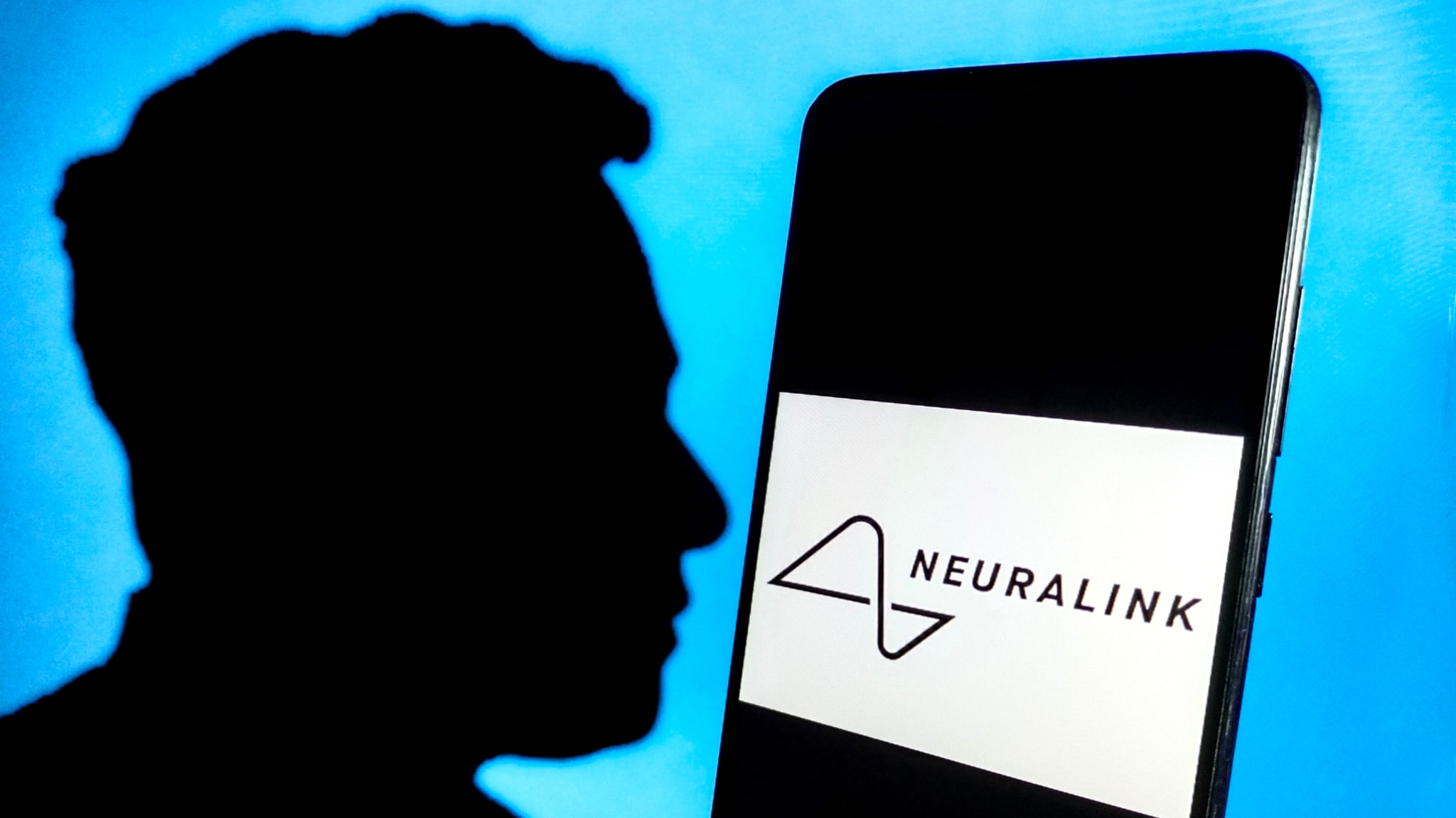 Silhouette of a person next to a smartphone displaying the Neuralink logo