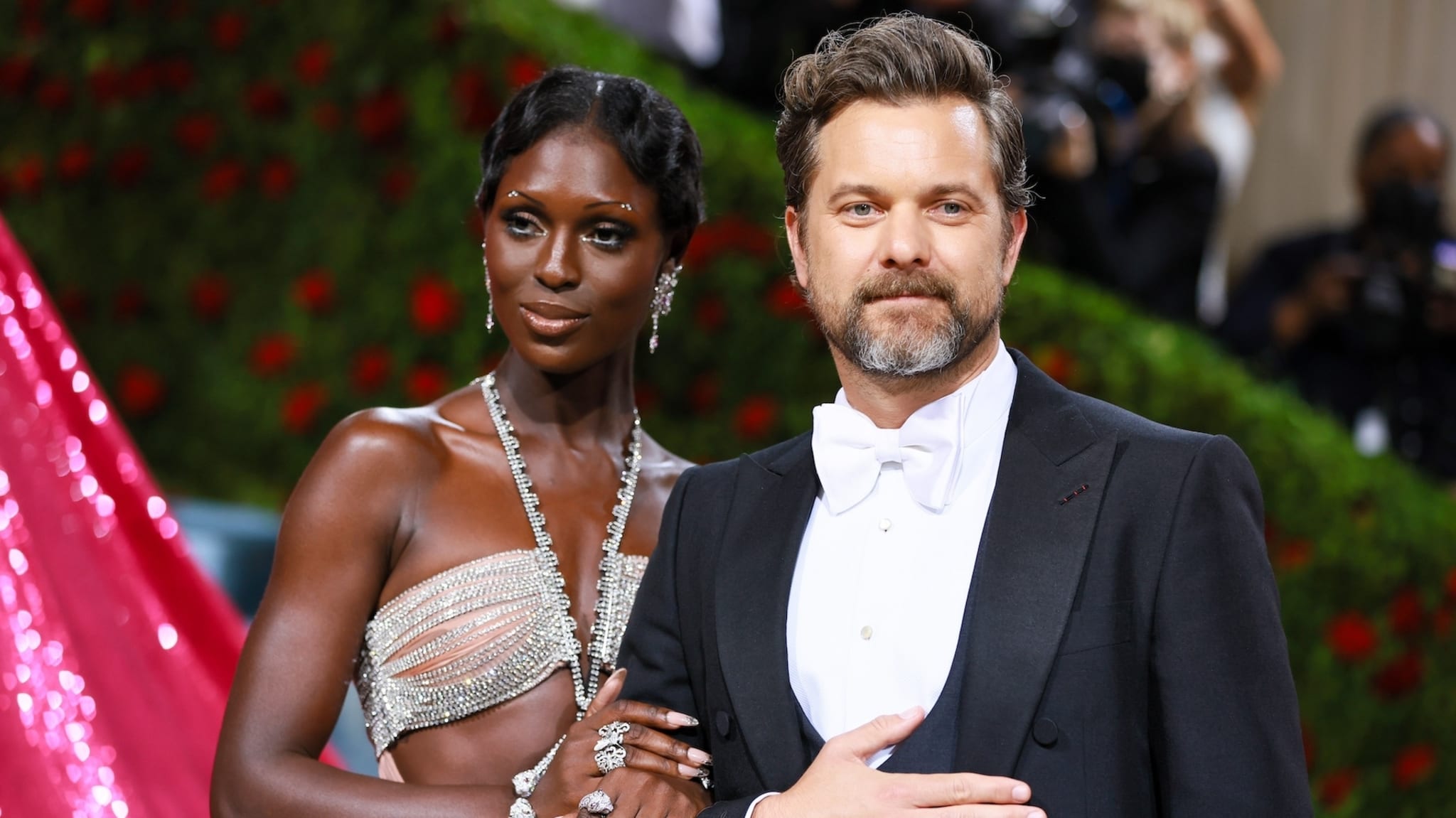 Jodie Turner-Smith in an embellished, cut-out dress with Joshua Jackson in a black tuxedo, posing on a red carpet
