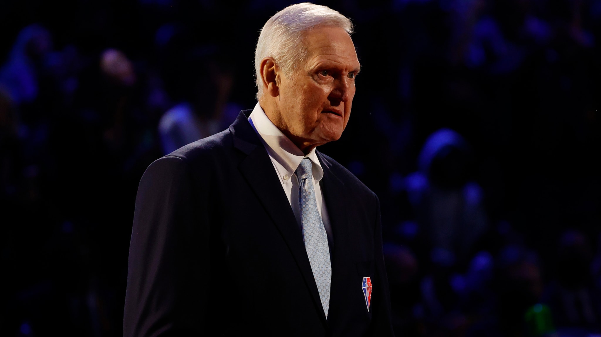 Jerry West in a suit with a light tie, standing in an indoor setting