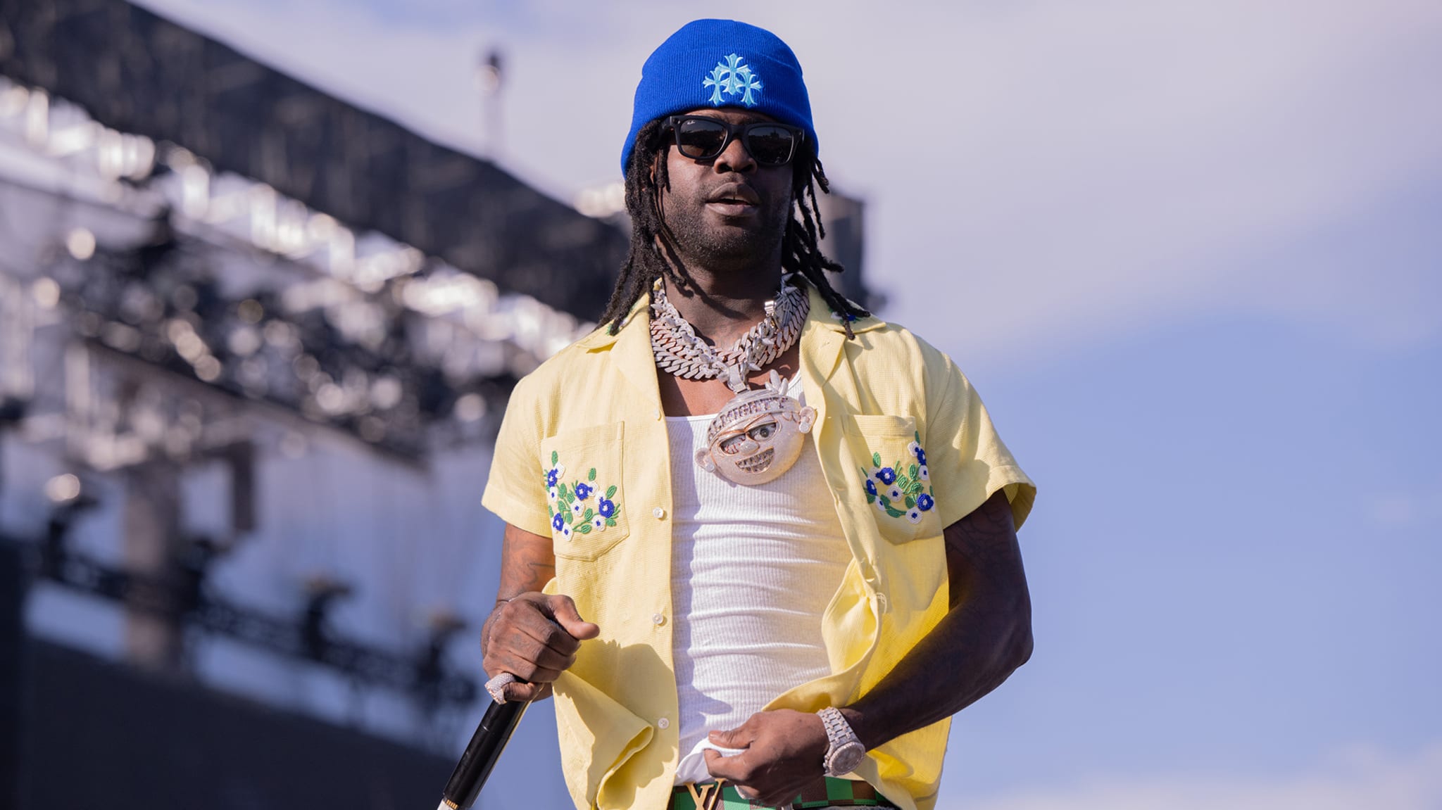 Man in a yellow patterned shirt and sunglasses performing on stage