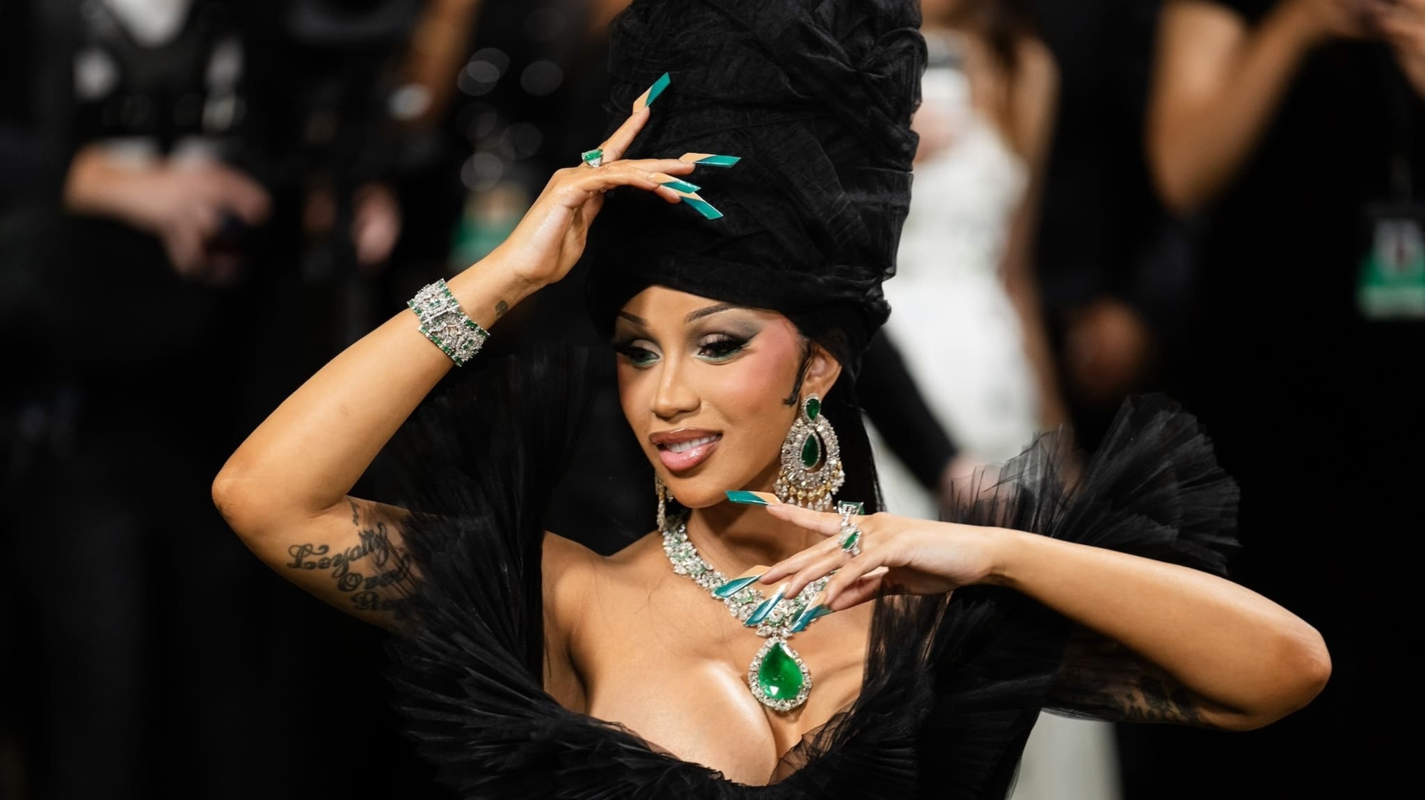 Cardi B in an extravagant black outfit with a large headpiece and statement jewelry at an event