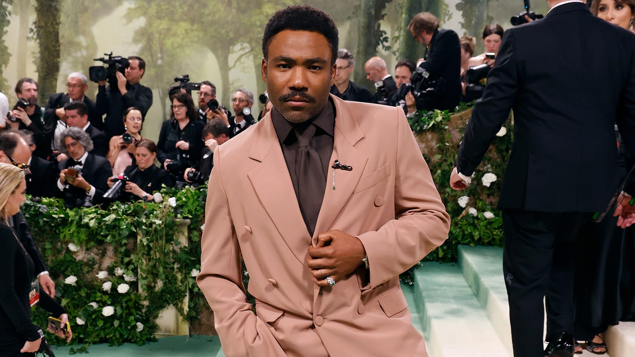 Man in elegant pink suit with photographers in background; fashion at a music event