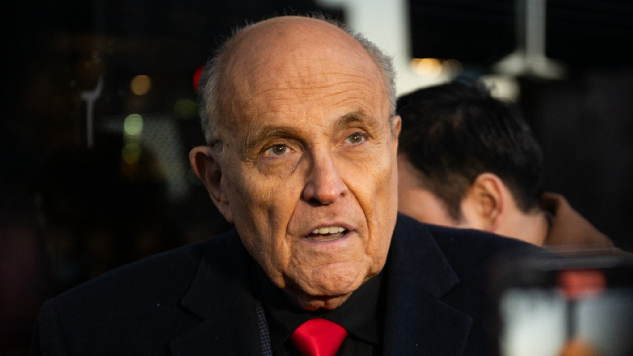 Rudy Giuliani wearing a dark suit with a red tie