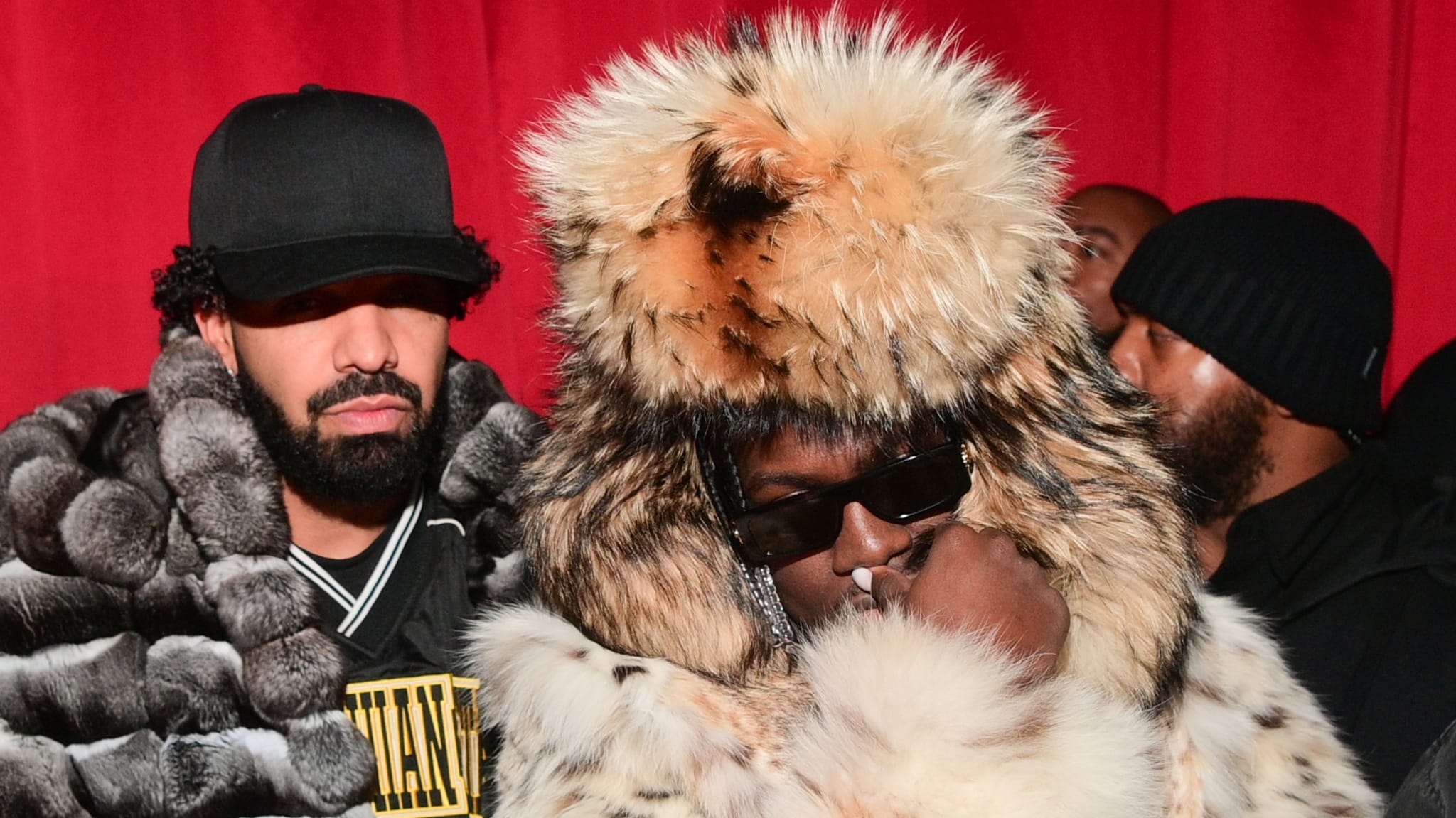 Drake in a black hat and jacket next to Lil Yachty in a large fur coat and hat, both at an event