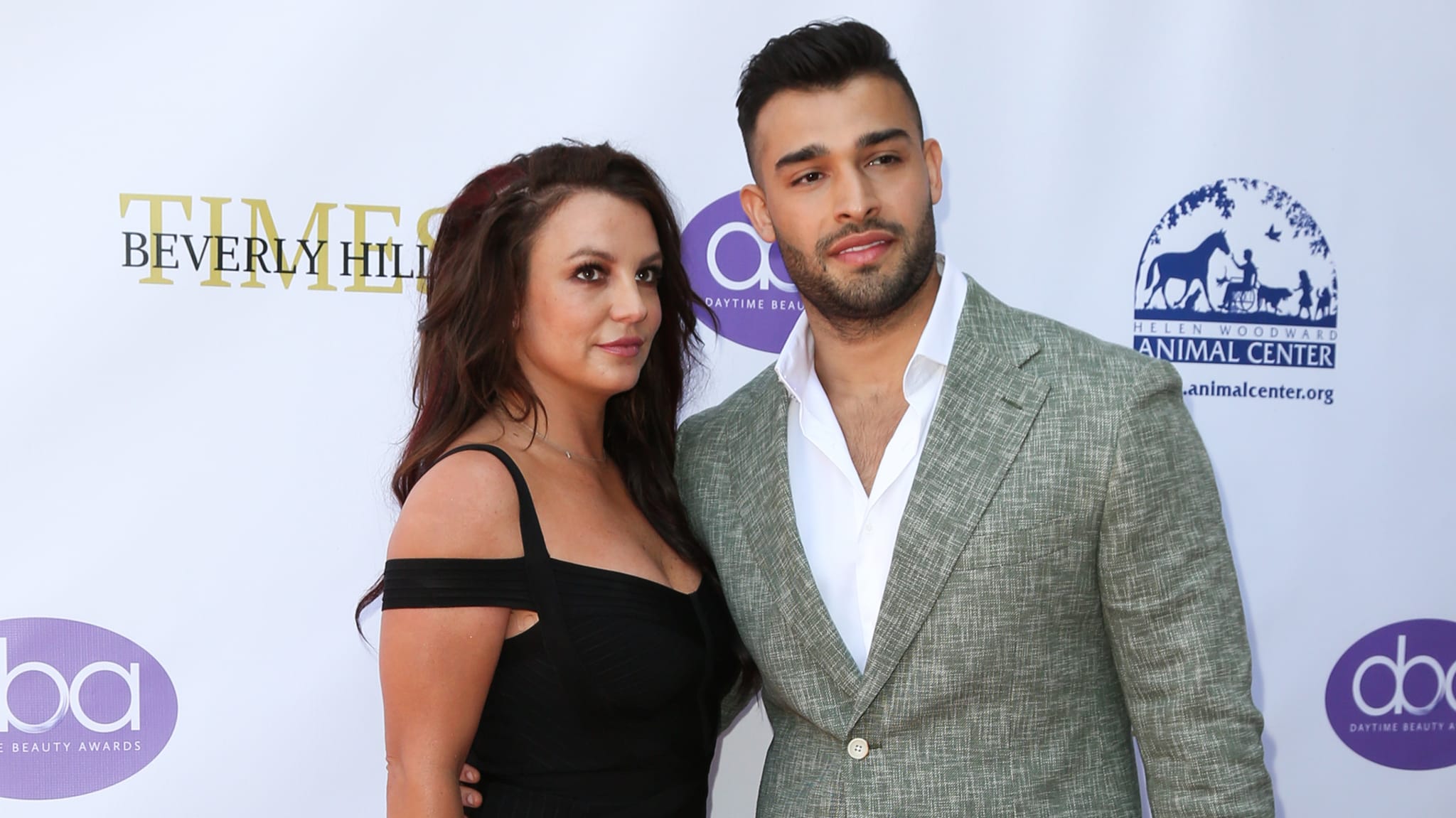 Two individuals posing together at an event; one wears a plunging neckline top and the other a patterned suit jacket