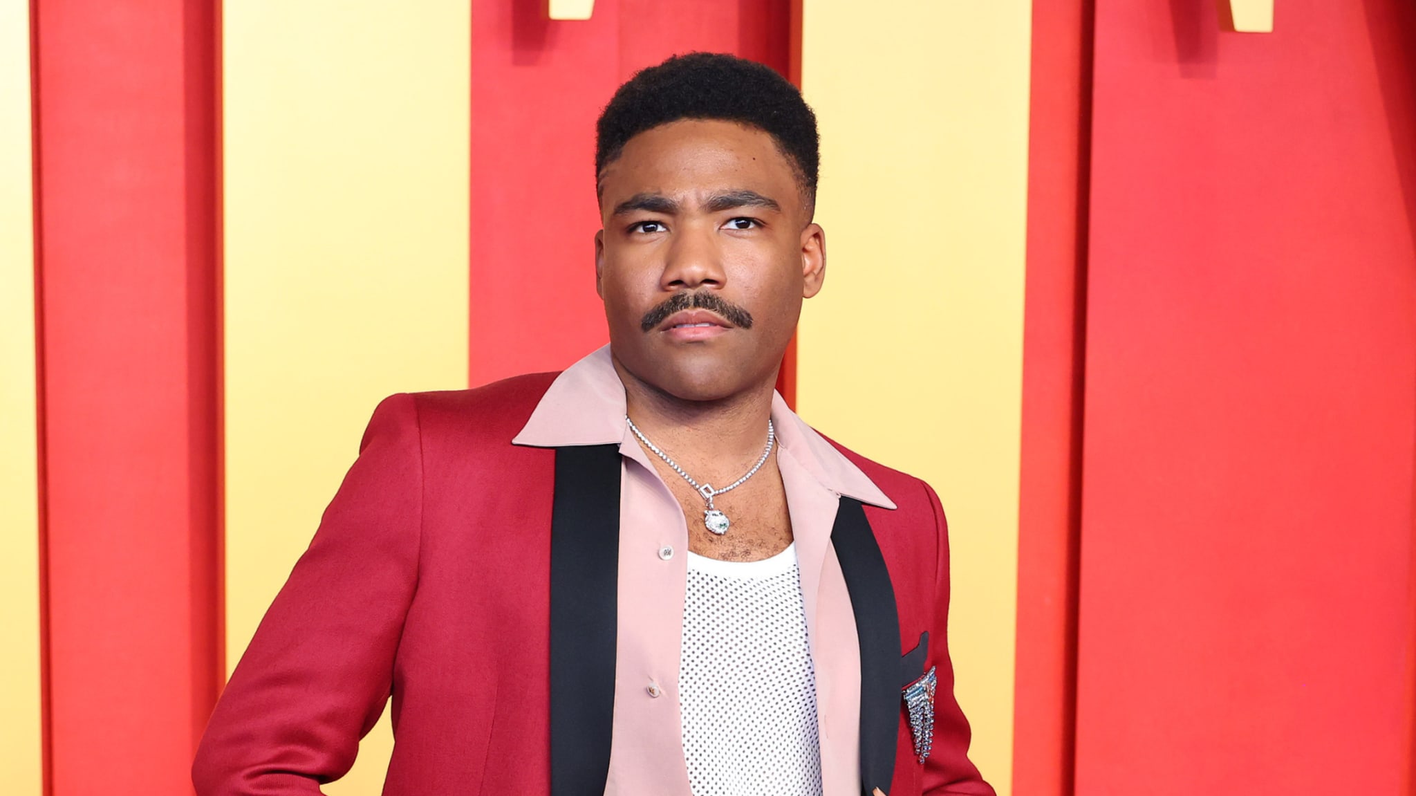 Man in a maroon suit jacket and white dotted shirt at an event