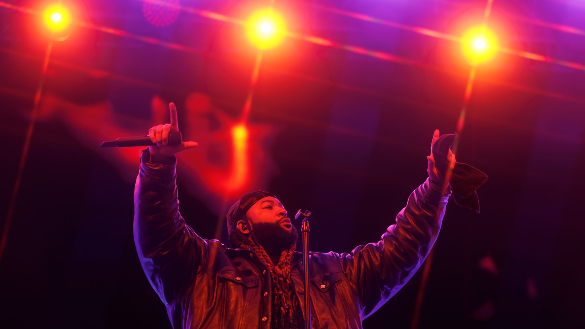 Musician on stage with microphone raised, performing under stage lights