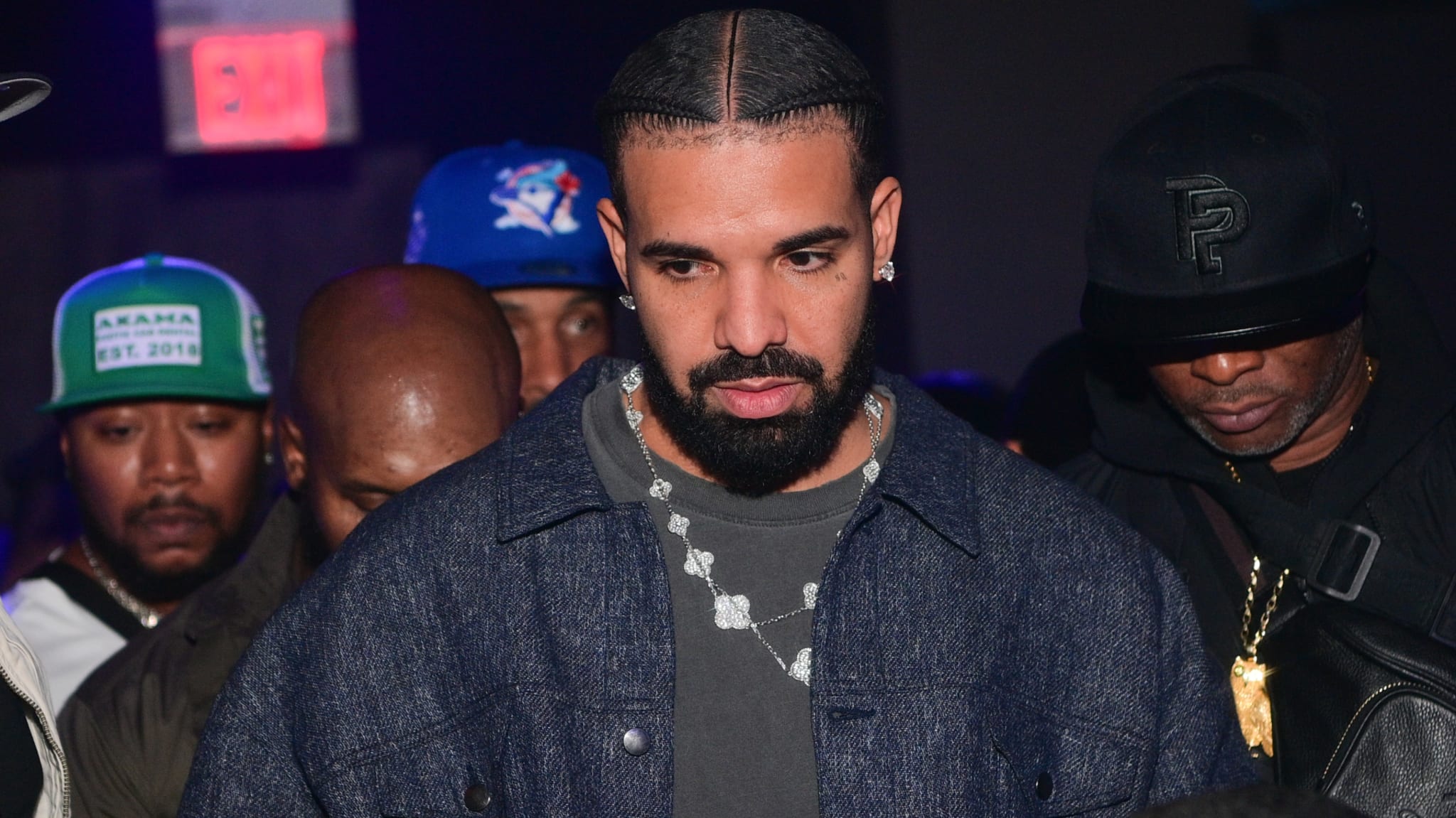 Music artist in a denim jacket, walking with security in a dim club setting