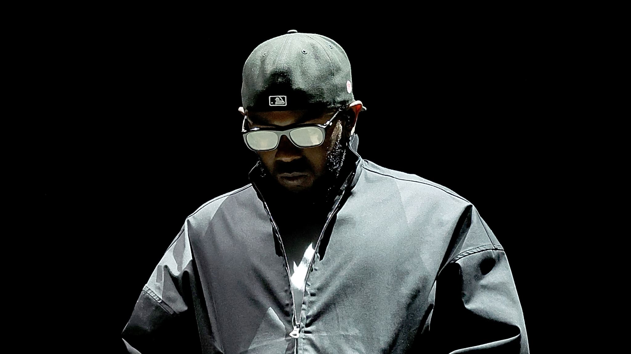 Man in sunglasses and cap, wearing a sporty jacket, on a stage