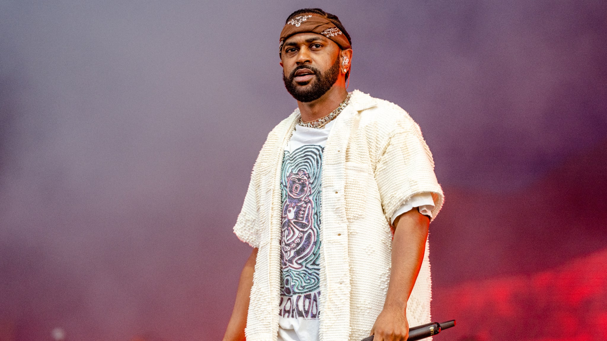 Music artist on stage performing, wearing a graphic tee and casual jacket, with a microphone in hand