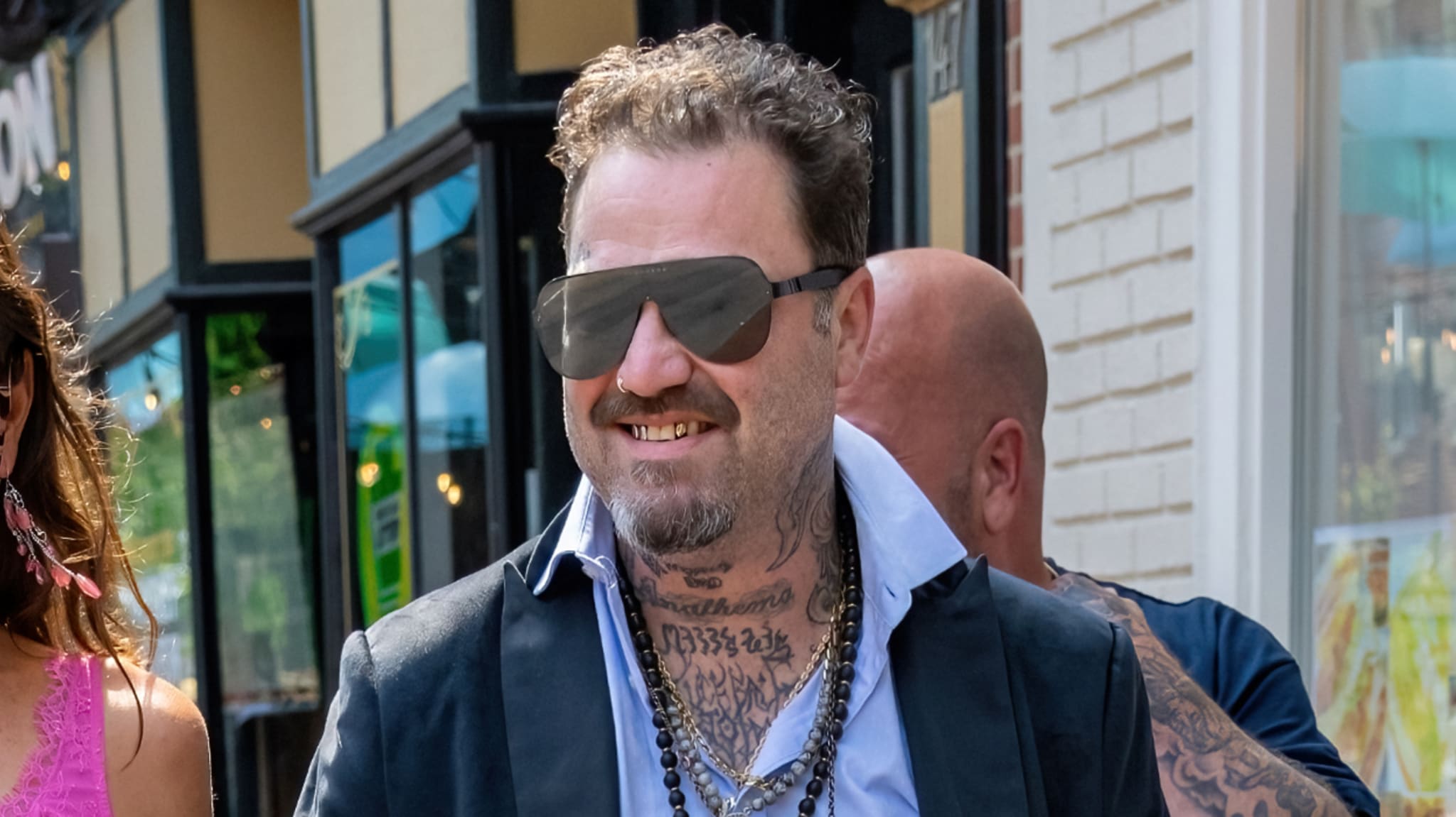 Bam Margera in sunglasses and tattooed, wearing a casual black outfit, walking outside