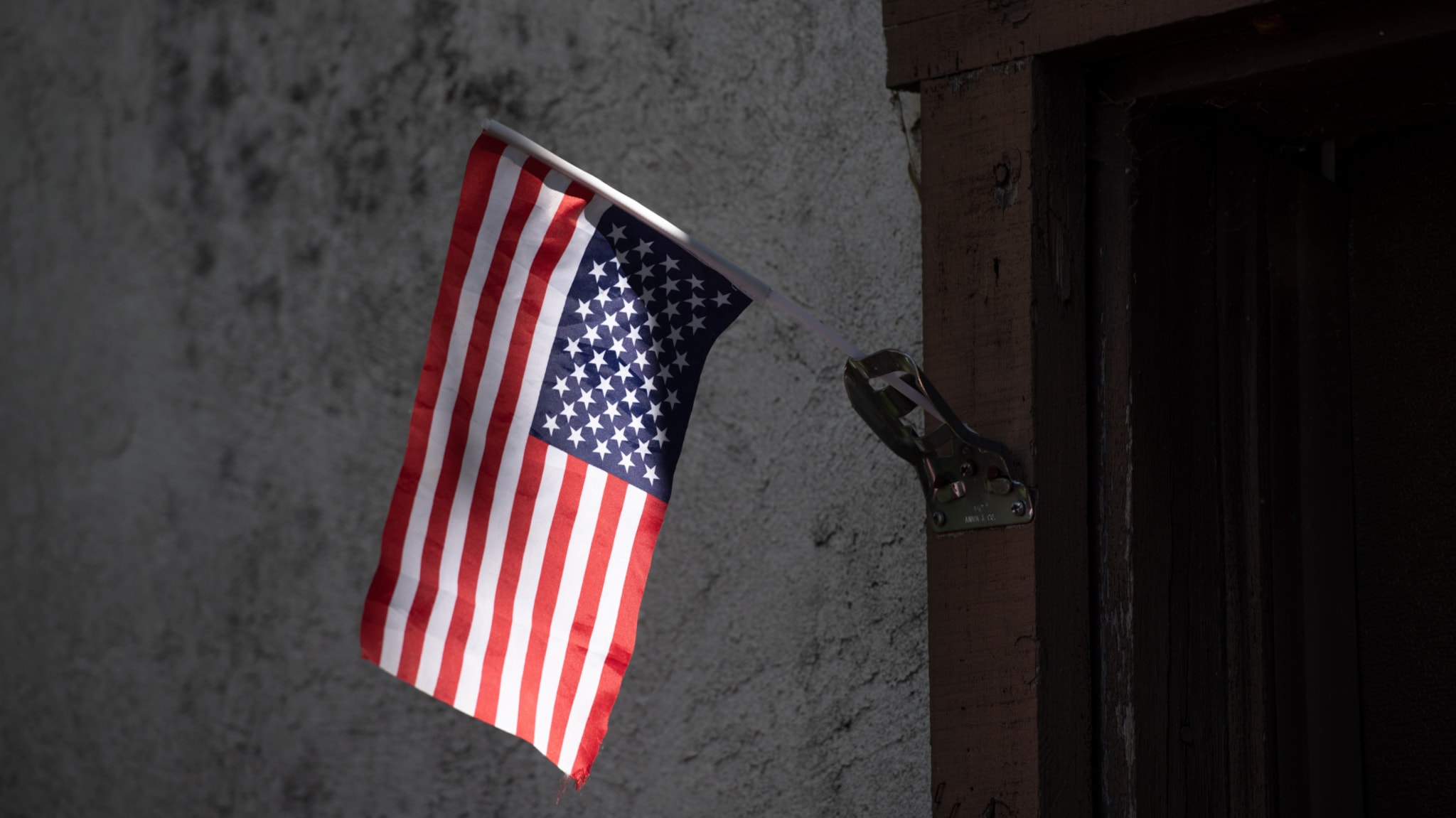 An upside-down American flag hangs from a metallic bracket on a textured wall