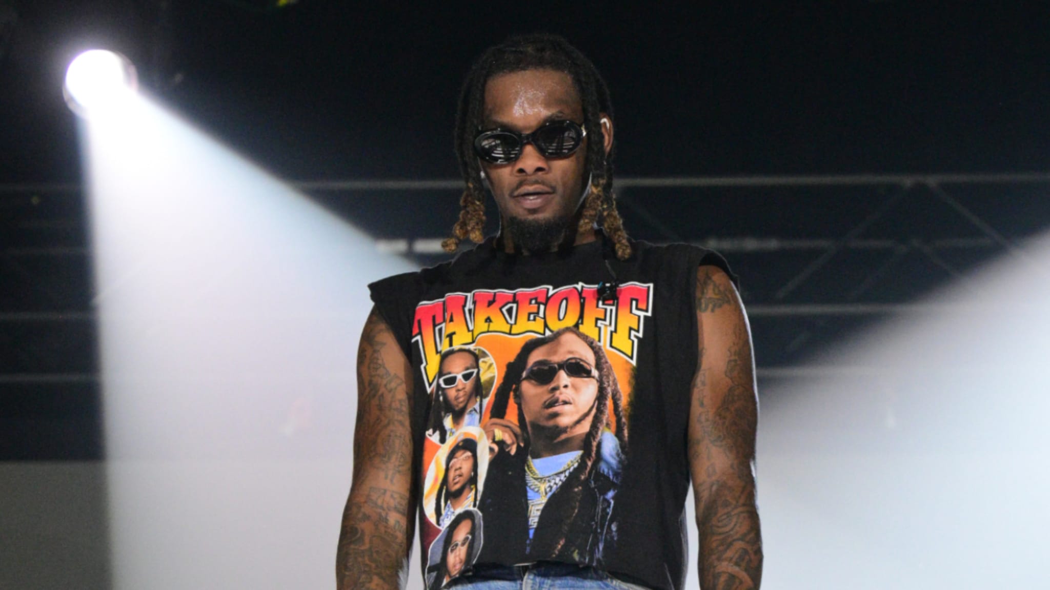 Offset on stage wearing a graphic tank top and sunglasses, with braided hair