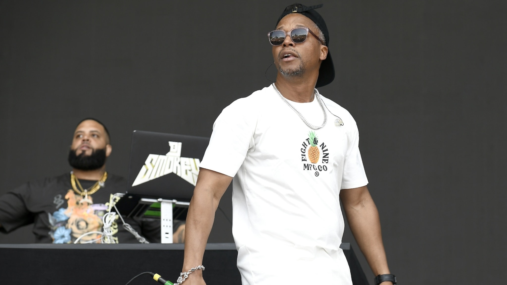 Two DJs performing on stage, one in a white shirt and cap and another partially obscured behind equipment