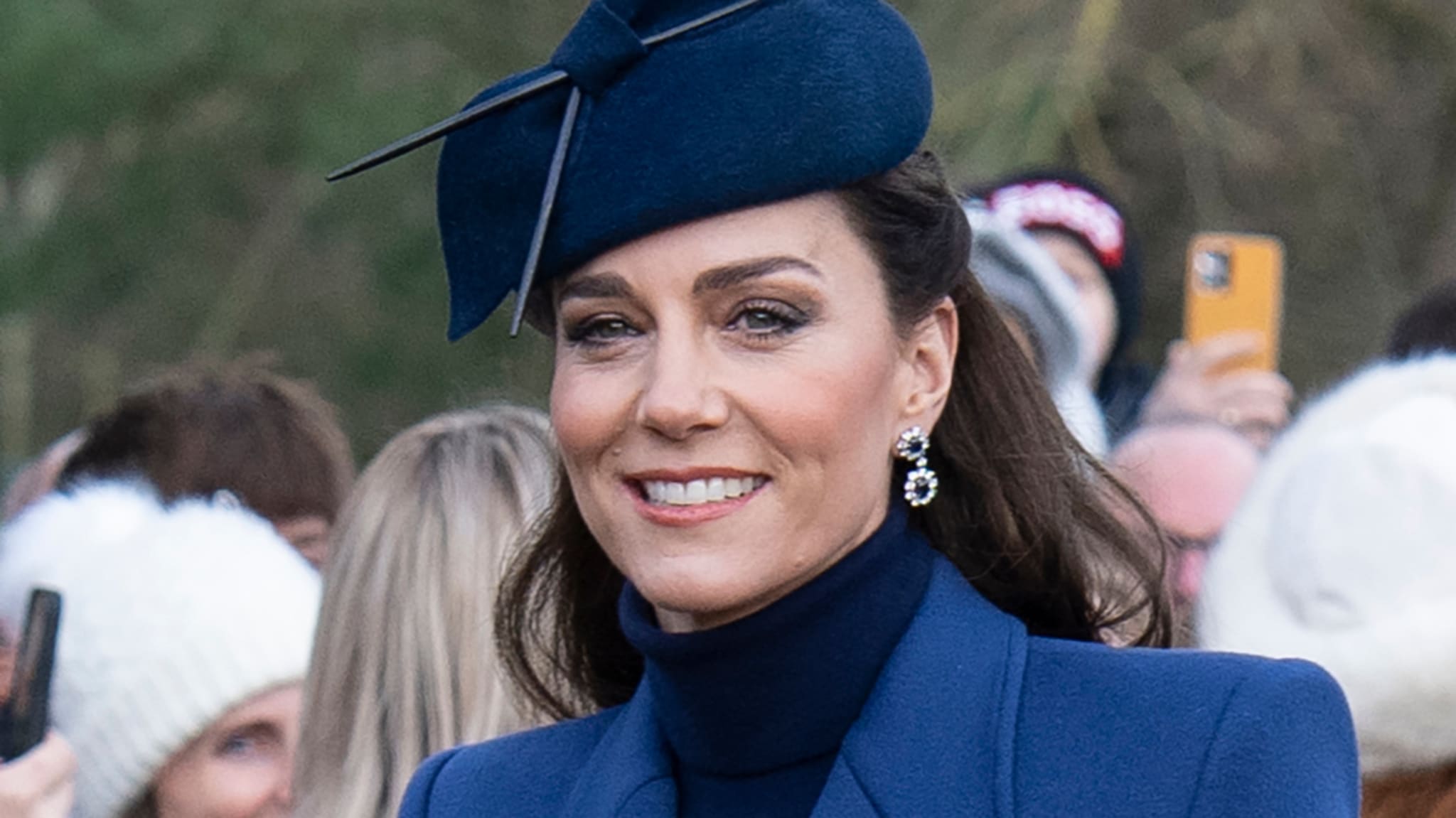 Kate in a hat and navy coat at a public event, smiling