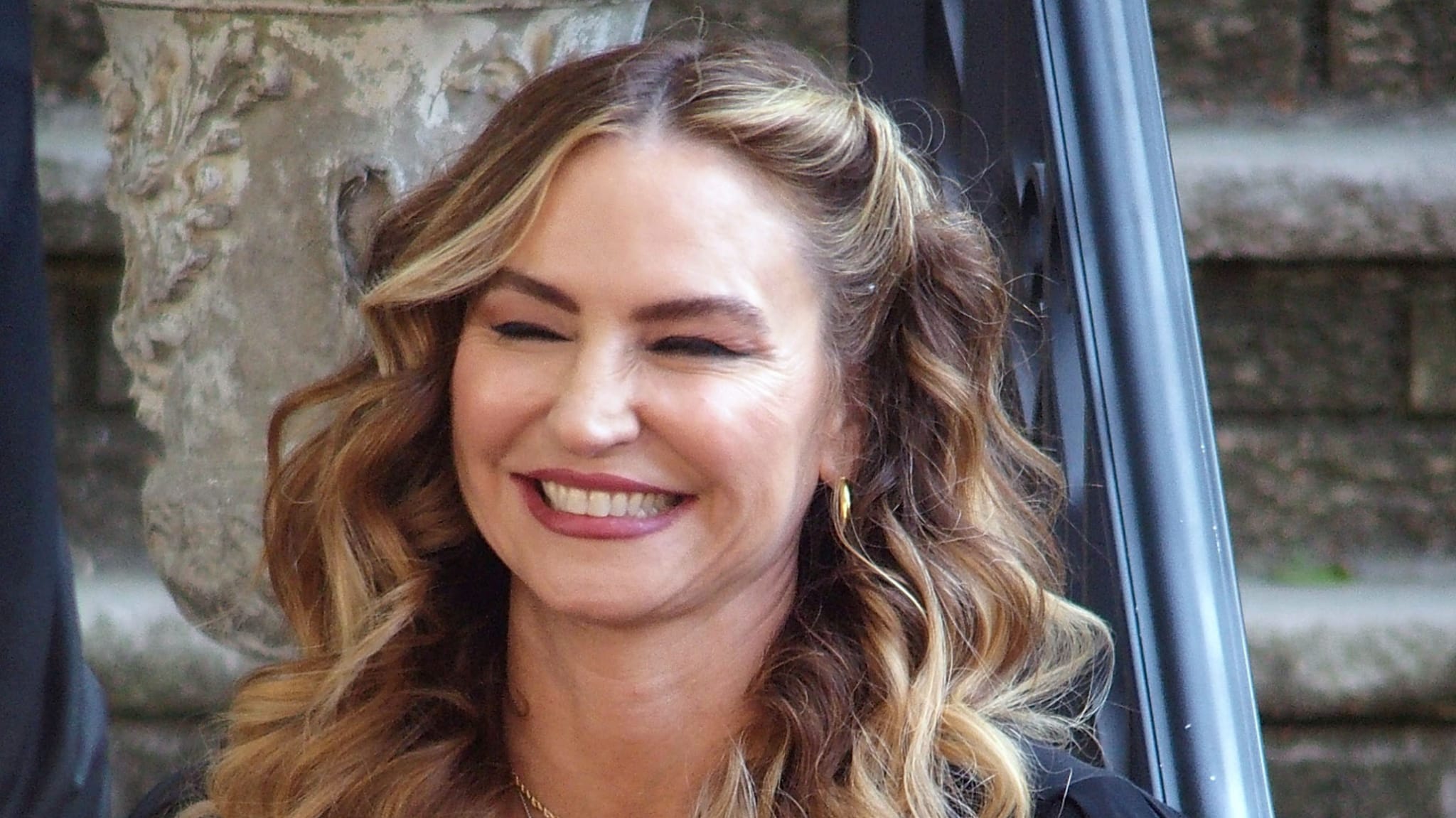 Smiling woman with long wavy hair, wearing earrings and a simple top