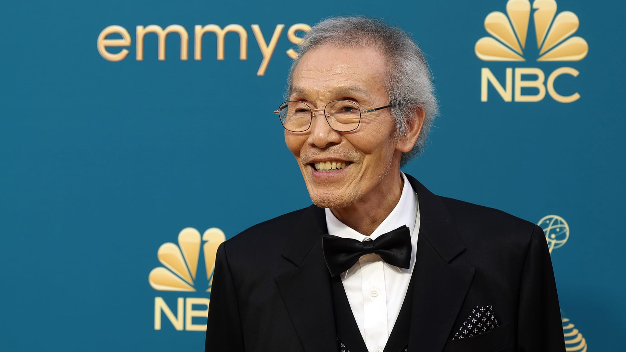 Elderly man in a black tuxedo smiling on the Emmy Awards red carpet