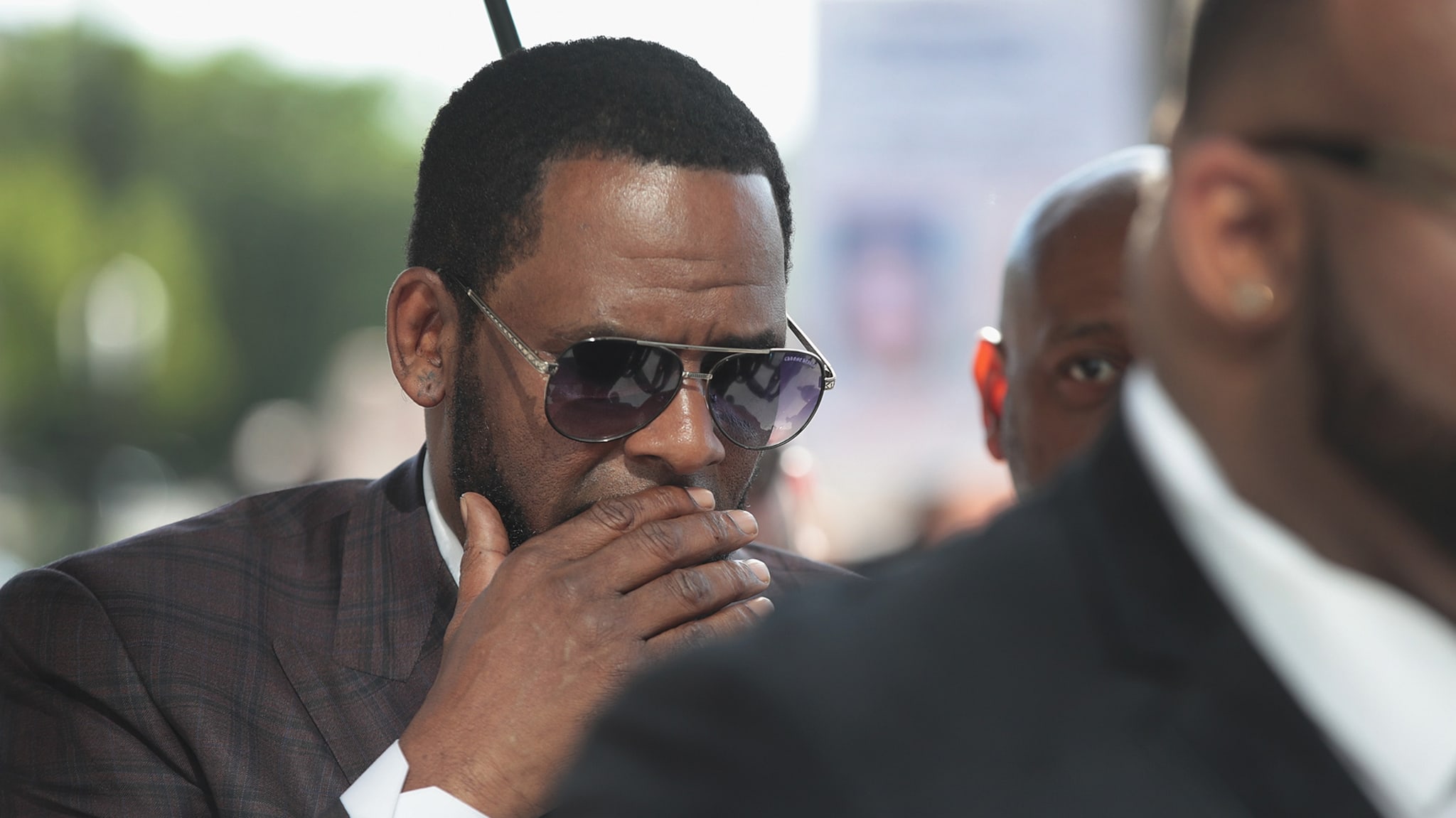 R. Kelly covers his mouth as he speaks to members of his entourage as he arrives at the Leighton Criminal Courts Building