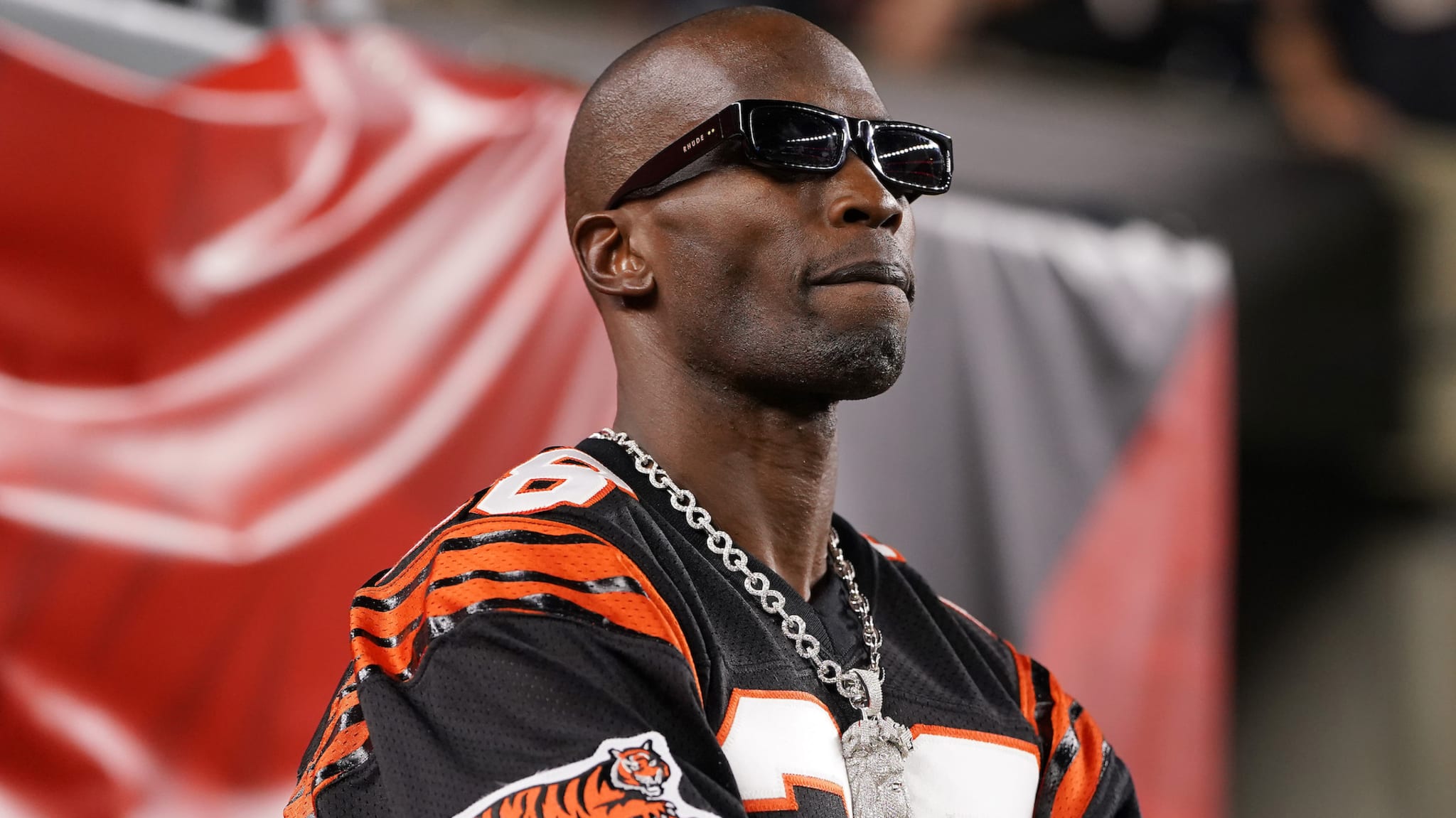 Chad Ochocinco, wearing sunglasses and a Cincinnati Bengals jersey, stands confidently with a chain around his neck.