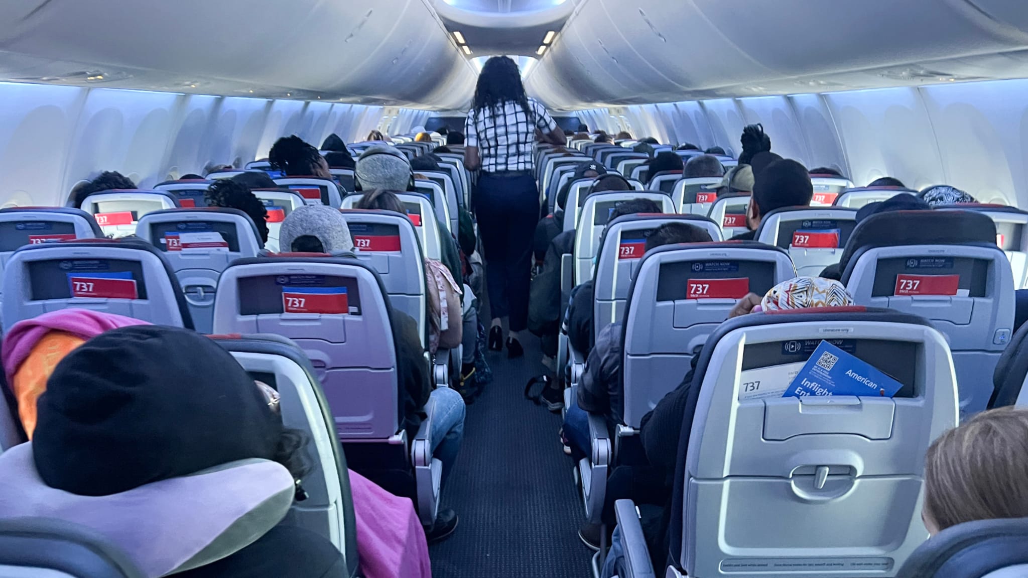 Interior of an airplane cabin with passengers seated and a flight attendant walking down the aisle.