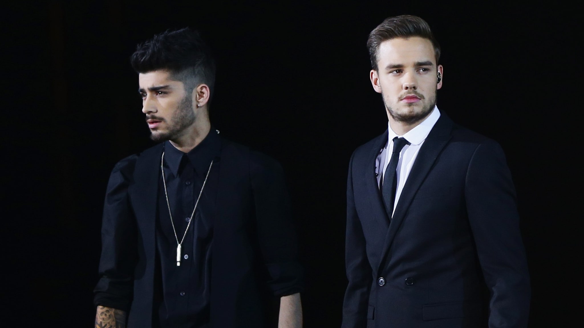 Zayn Malik and Liam Payne in suits, standing side by side against a dark background.