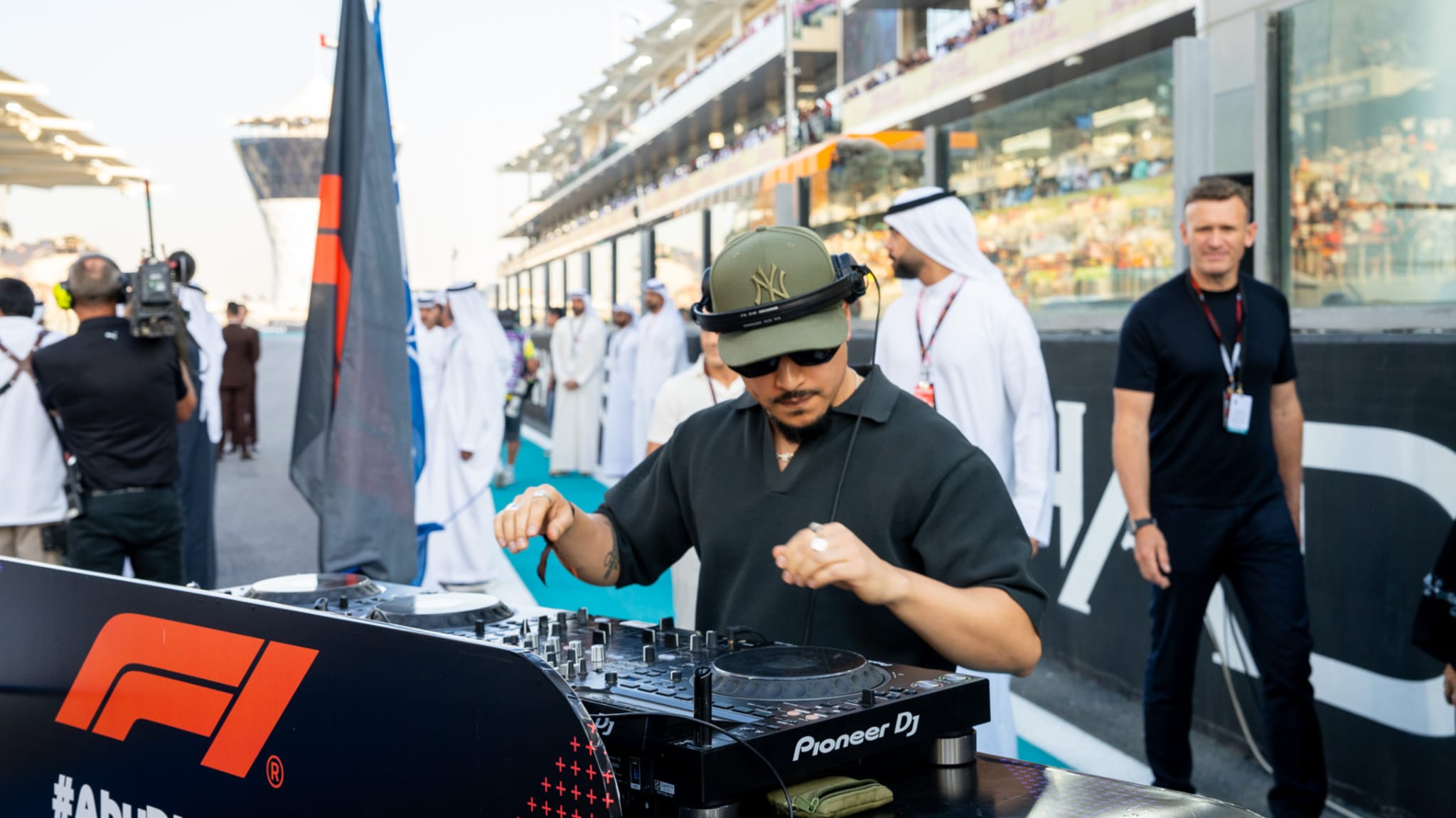 A DJ performing at a Formula 1 event, with people in traditional Middle Eastern attire and spectators in the background.