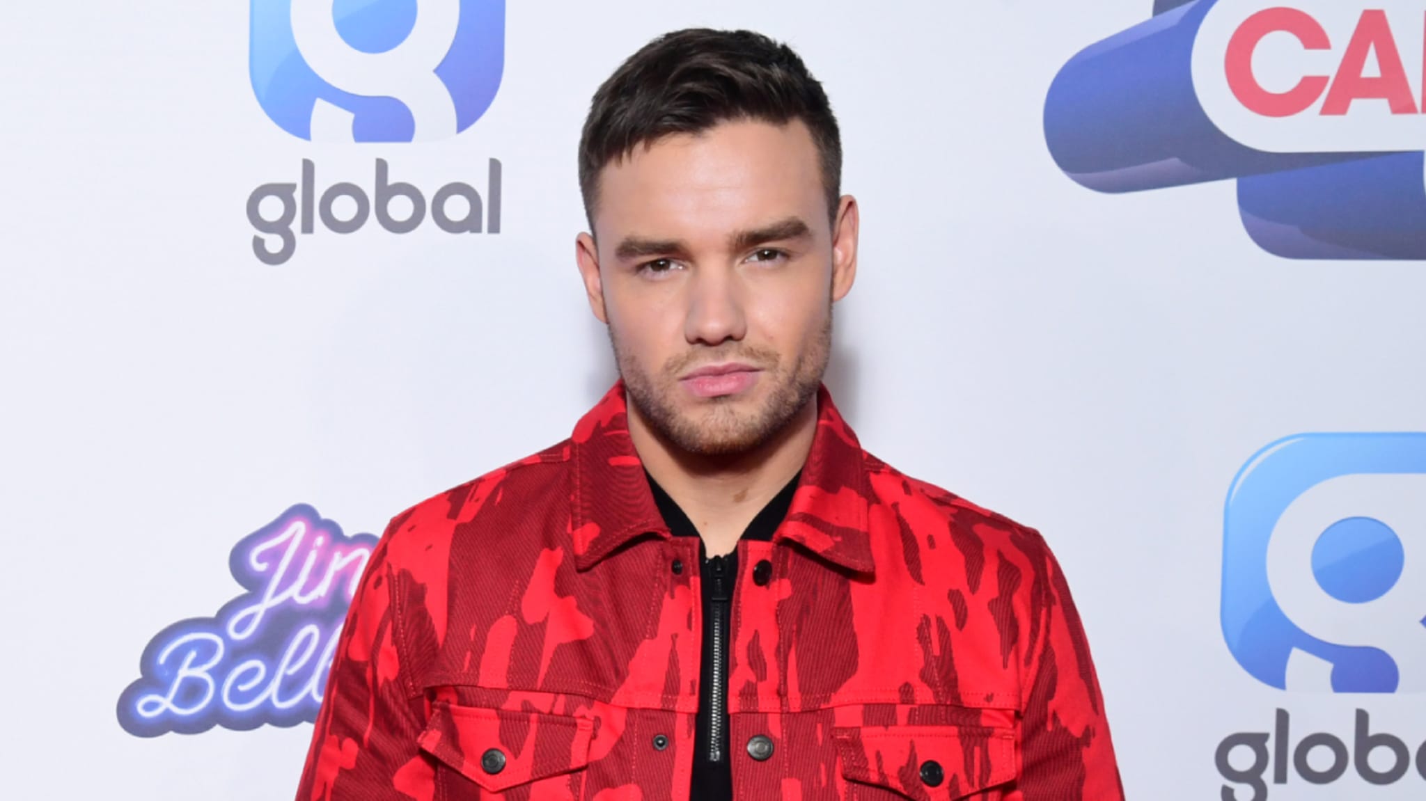 Liam Payne in a red jacket, posing.