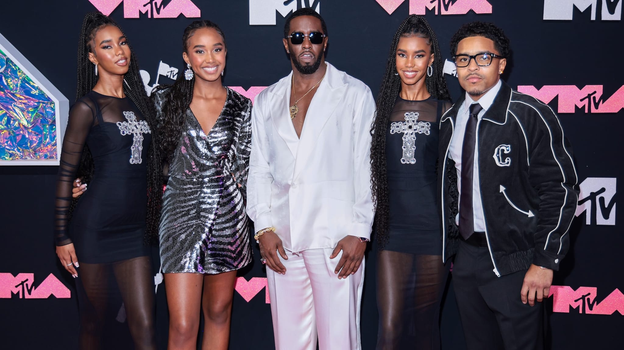 Sean "Diddy" Combs in a white suit with four people at the MTV event. The group poses on the red carpet with the MTV logo in the background.