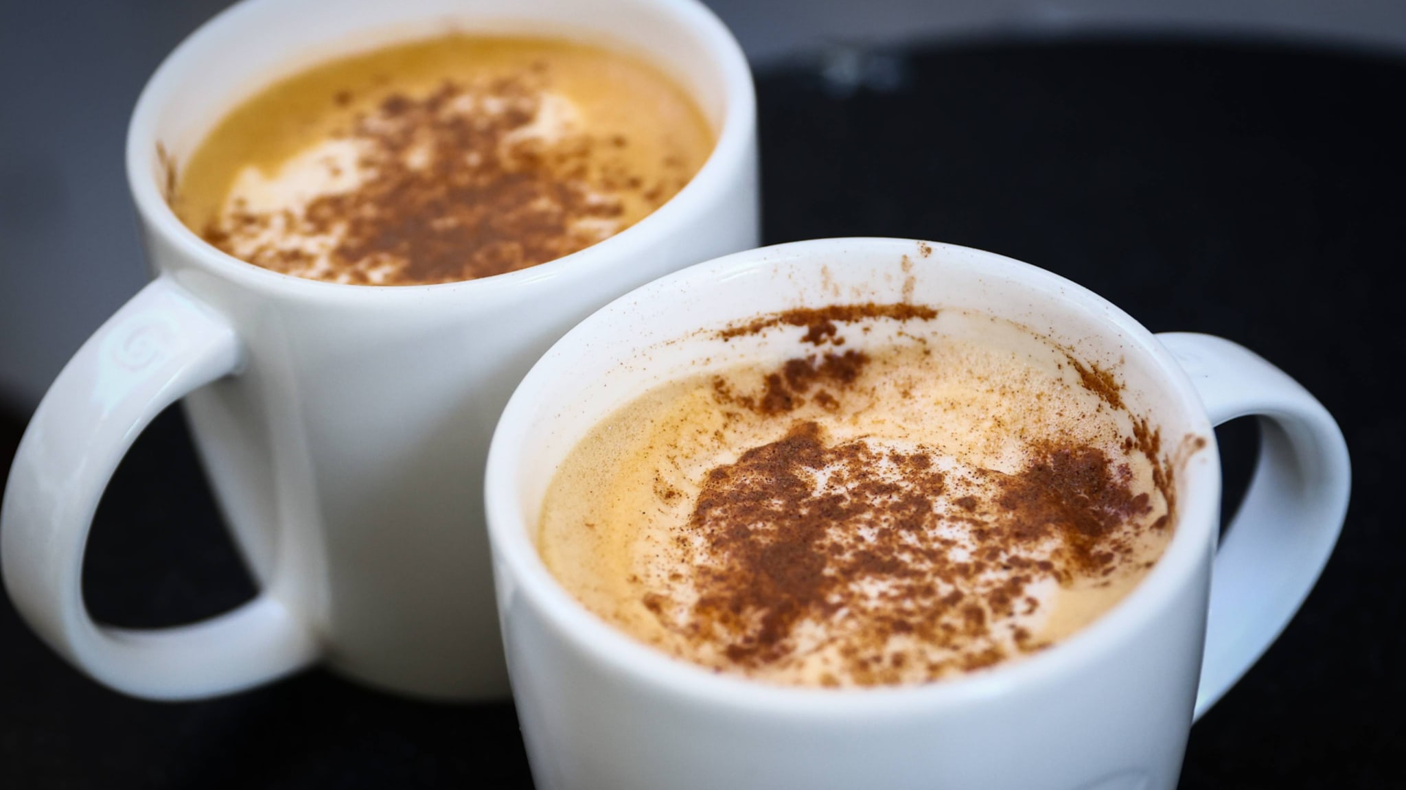 Two white mugs filled with frothy coffee topped with a sprinkle of cinnamon.