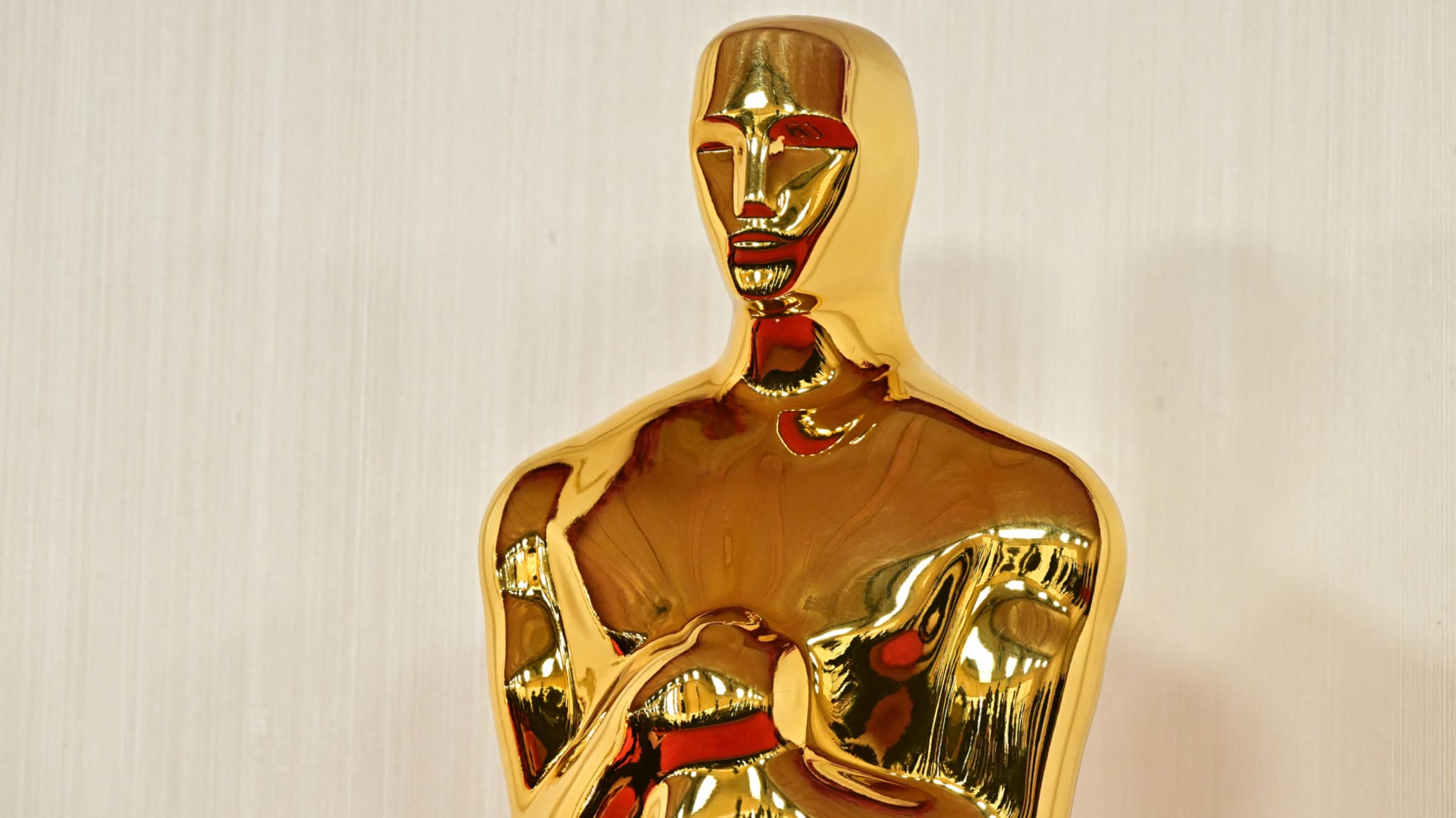 A close-up of a gold Oscar statuette against a light background.