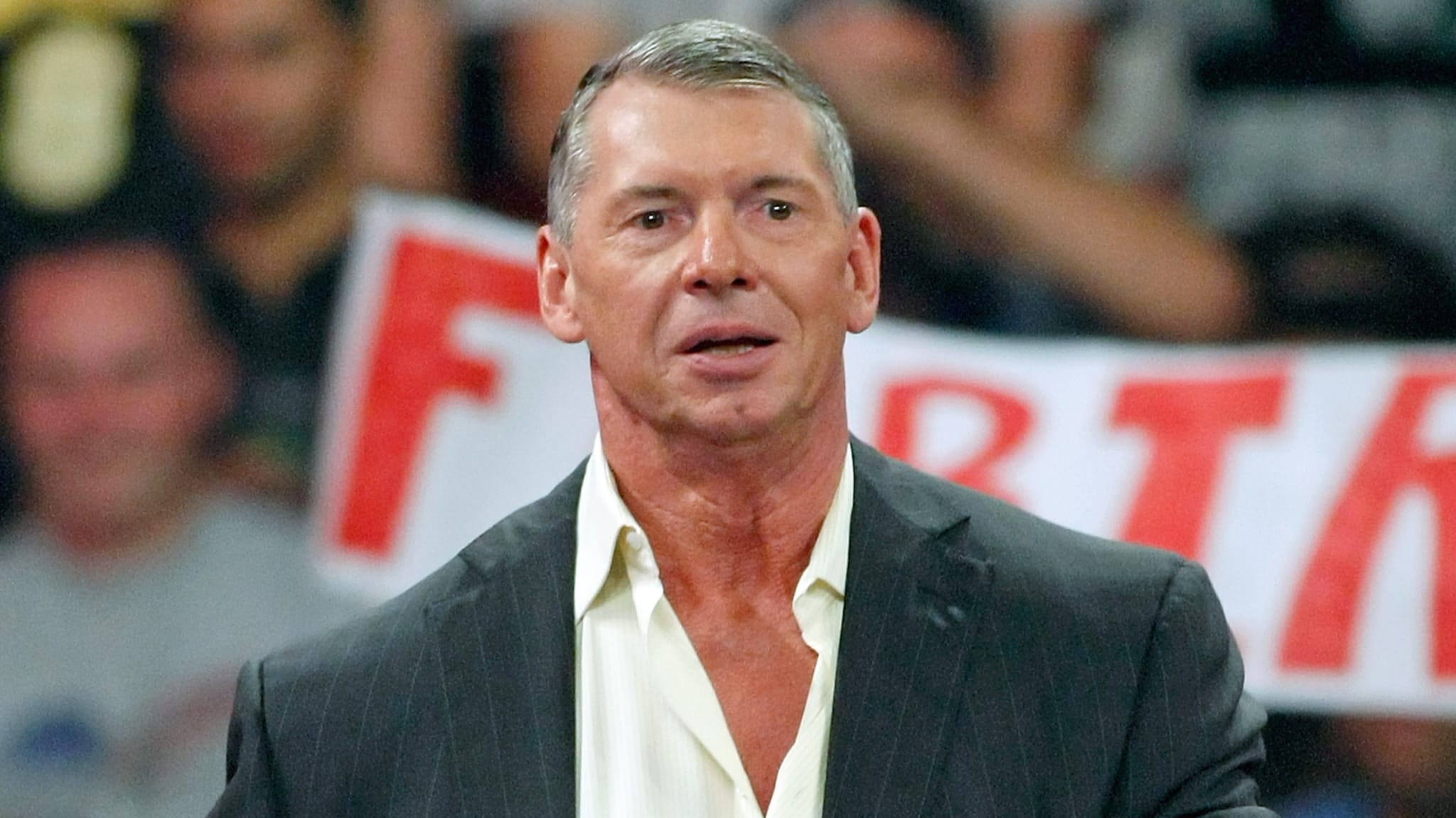 A man in a suit stands in front of a blurred crowd holding a sign.