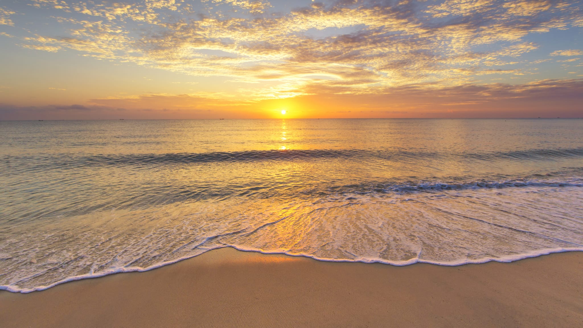 A serene beach scene at sunrise, with gentle waves lapping the sandy shore and a vibrant orange sky reflecting on the water.