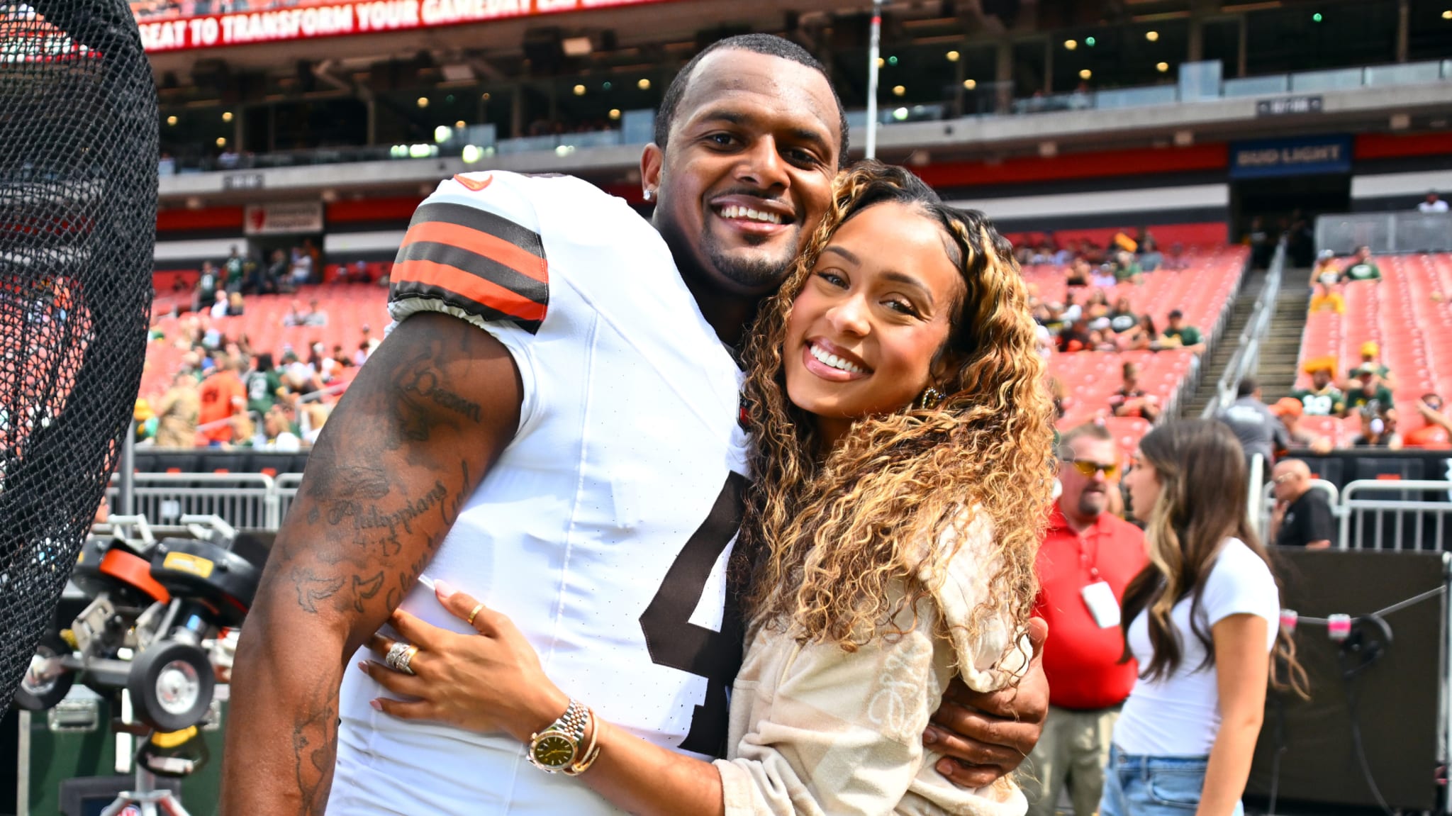 A man in a football uniform and a woman with curly hair smile and pose together in a stadium.