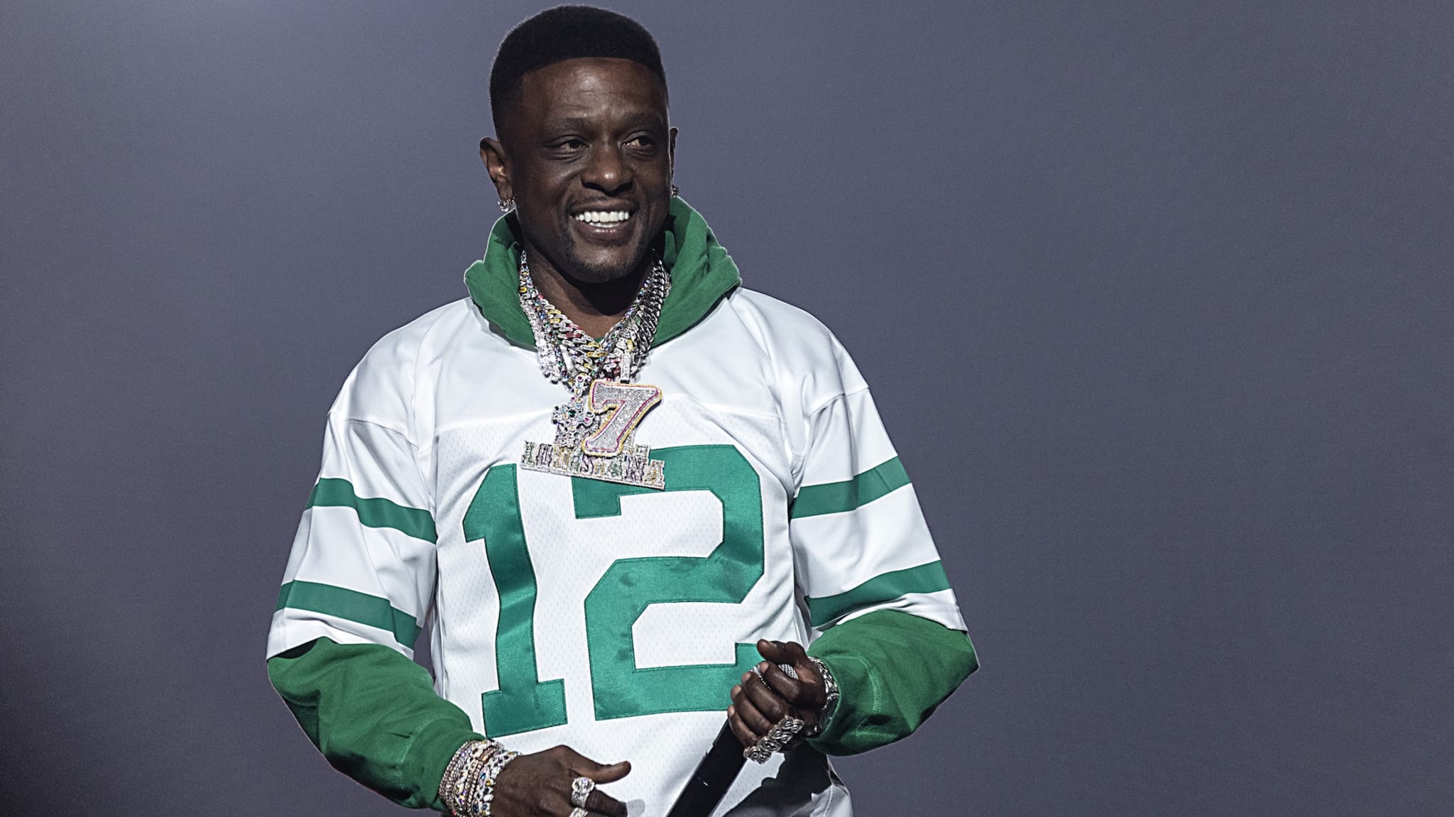 Rapper Boosie Badazz on stage wearing a white and green jersey with the number 12, multiple chains, and smiling.