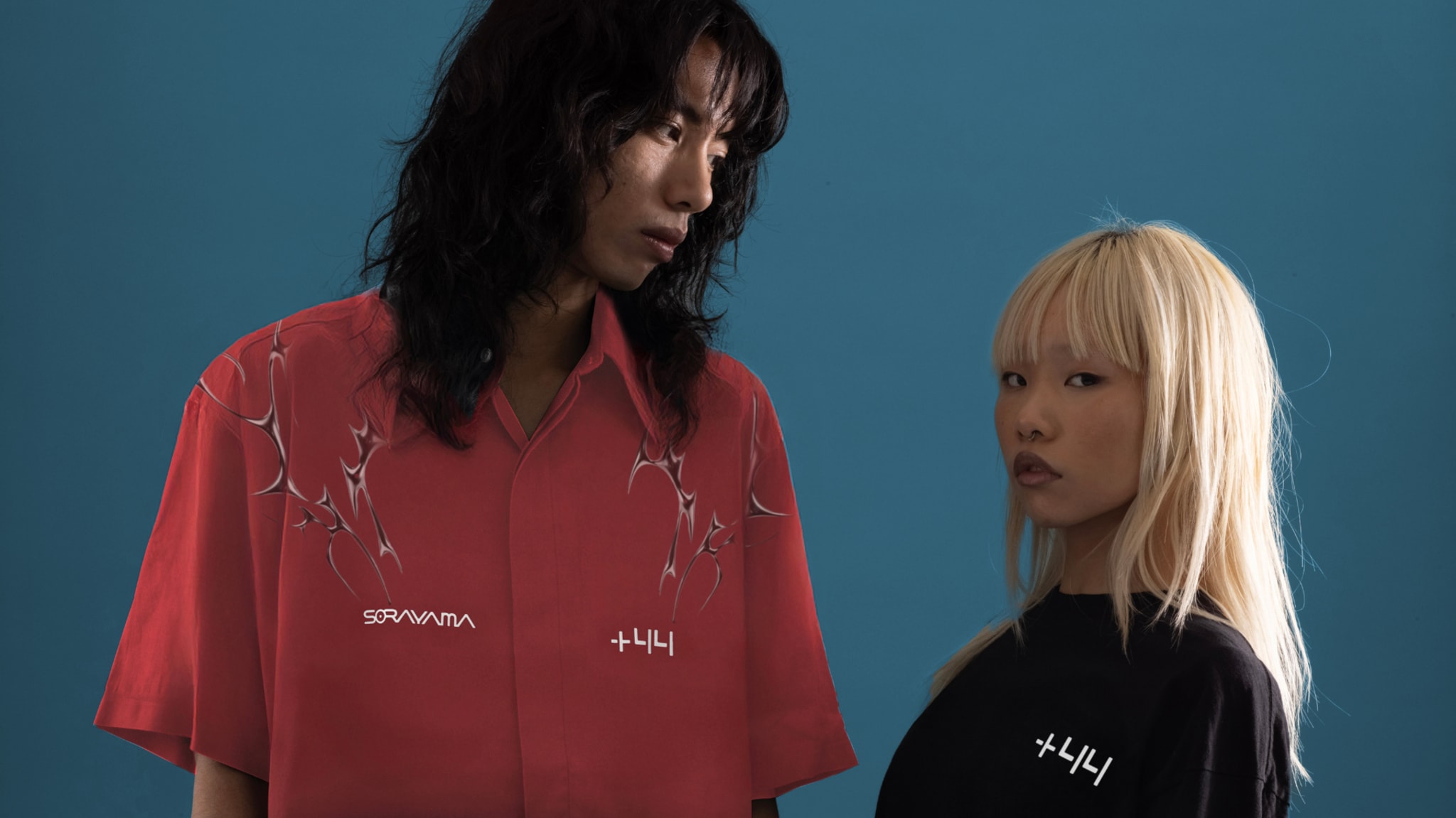Two models pose against a blue background. One wears a red shirt with patterns, the other a black shirt. Both shirts have white text.