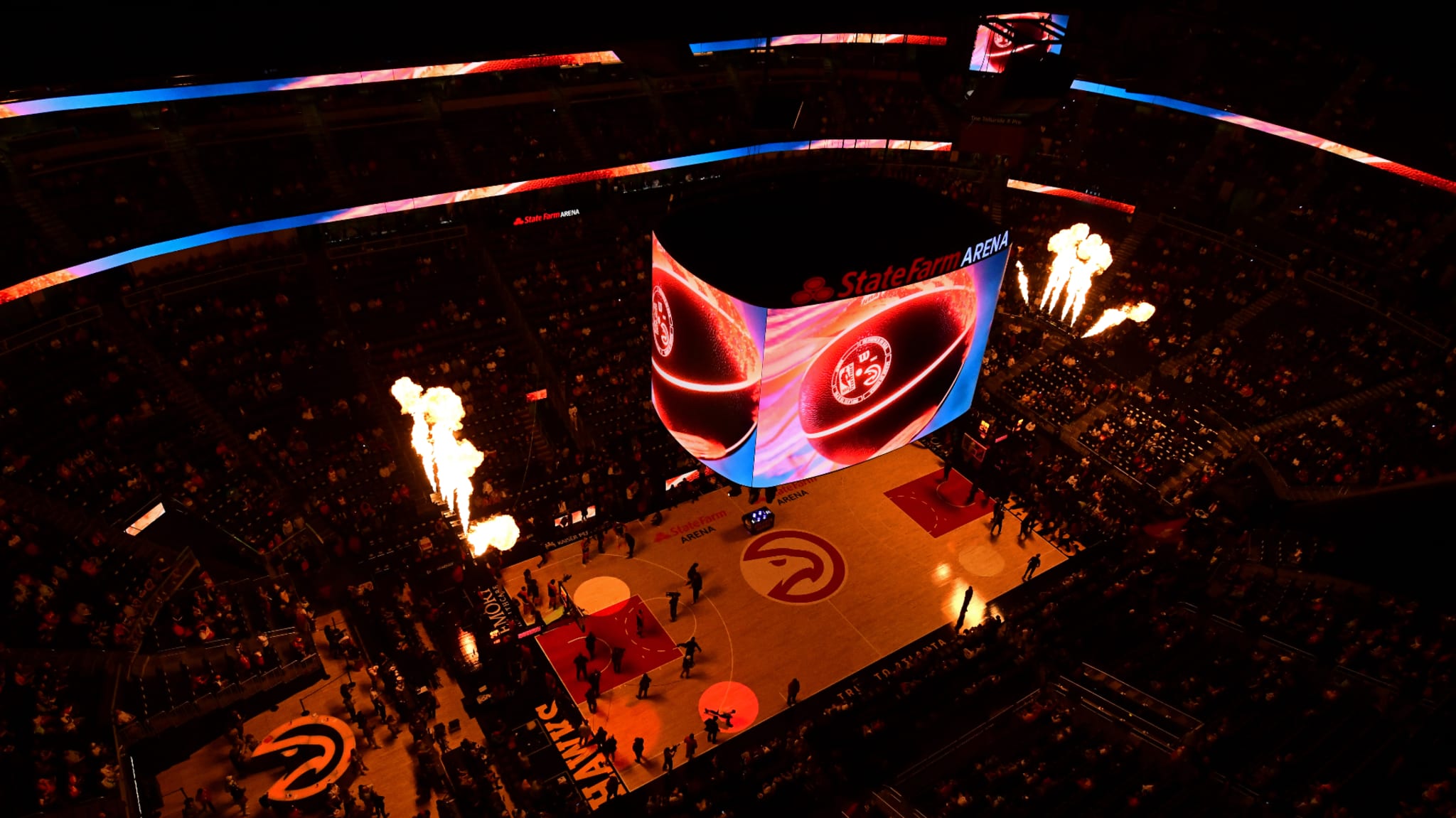 A basketball court at State Farm Arena, with a large screen displaying graphics and flames shooting up, surrounded by a crowd.