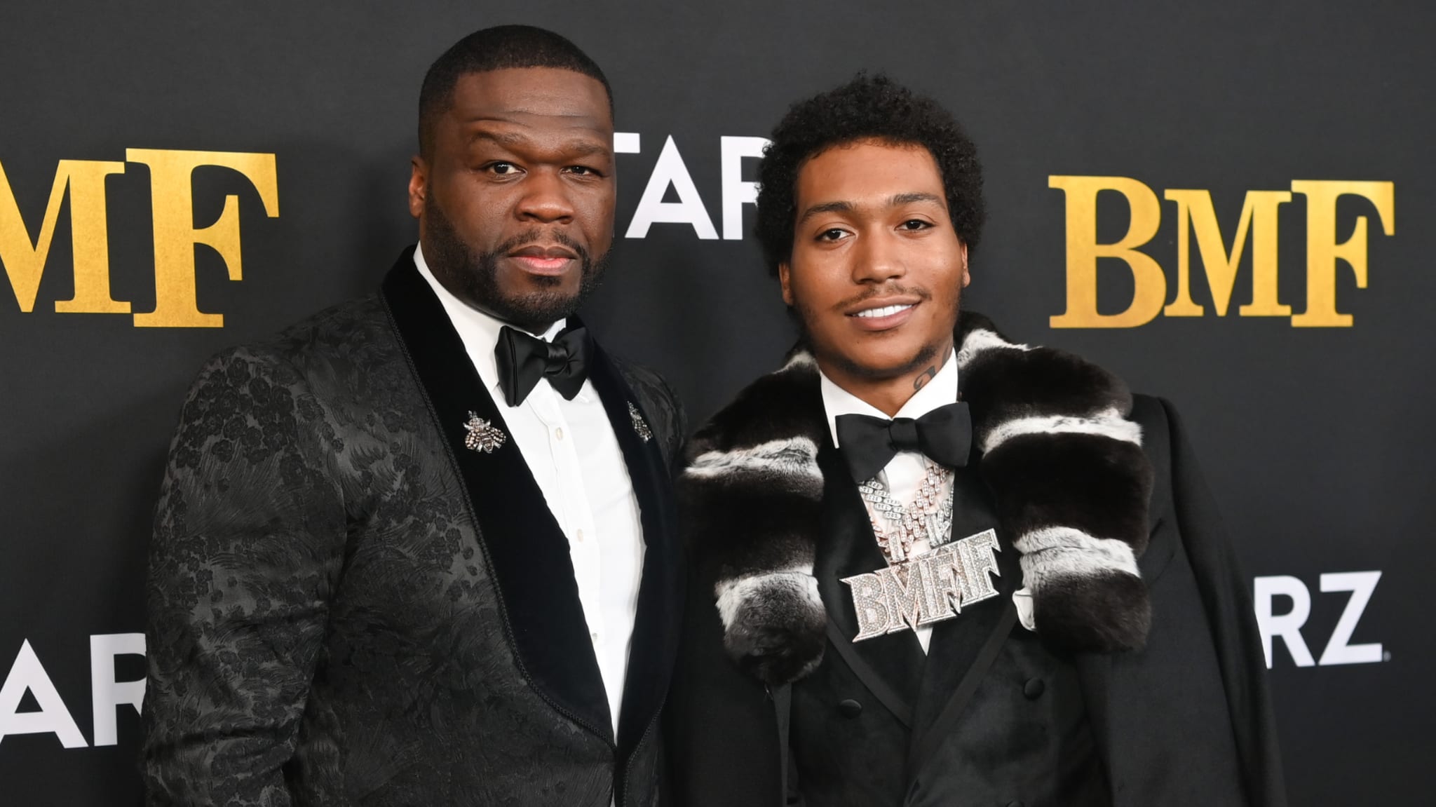 50 Cent and Demetrius "Lil Meech" Flenory Jr. at the "BMF" premiere, dressed in formal wear, standing against a branded backdrop.