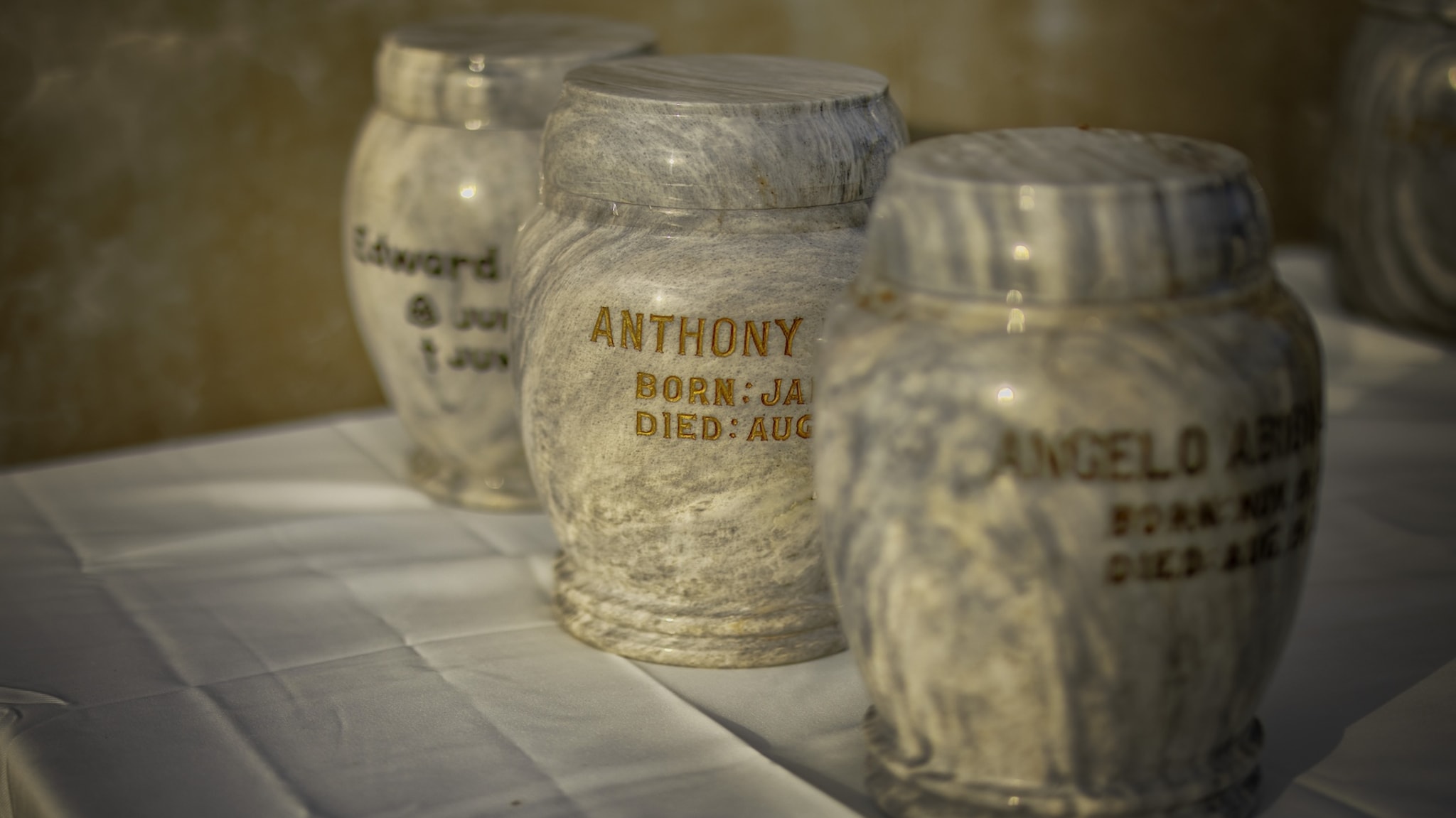 Marble urns with engraved names and dates on a table, casting soft shadows in warm light.