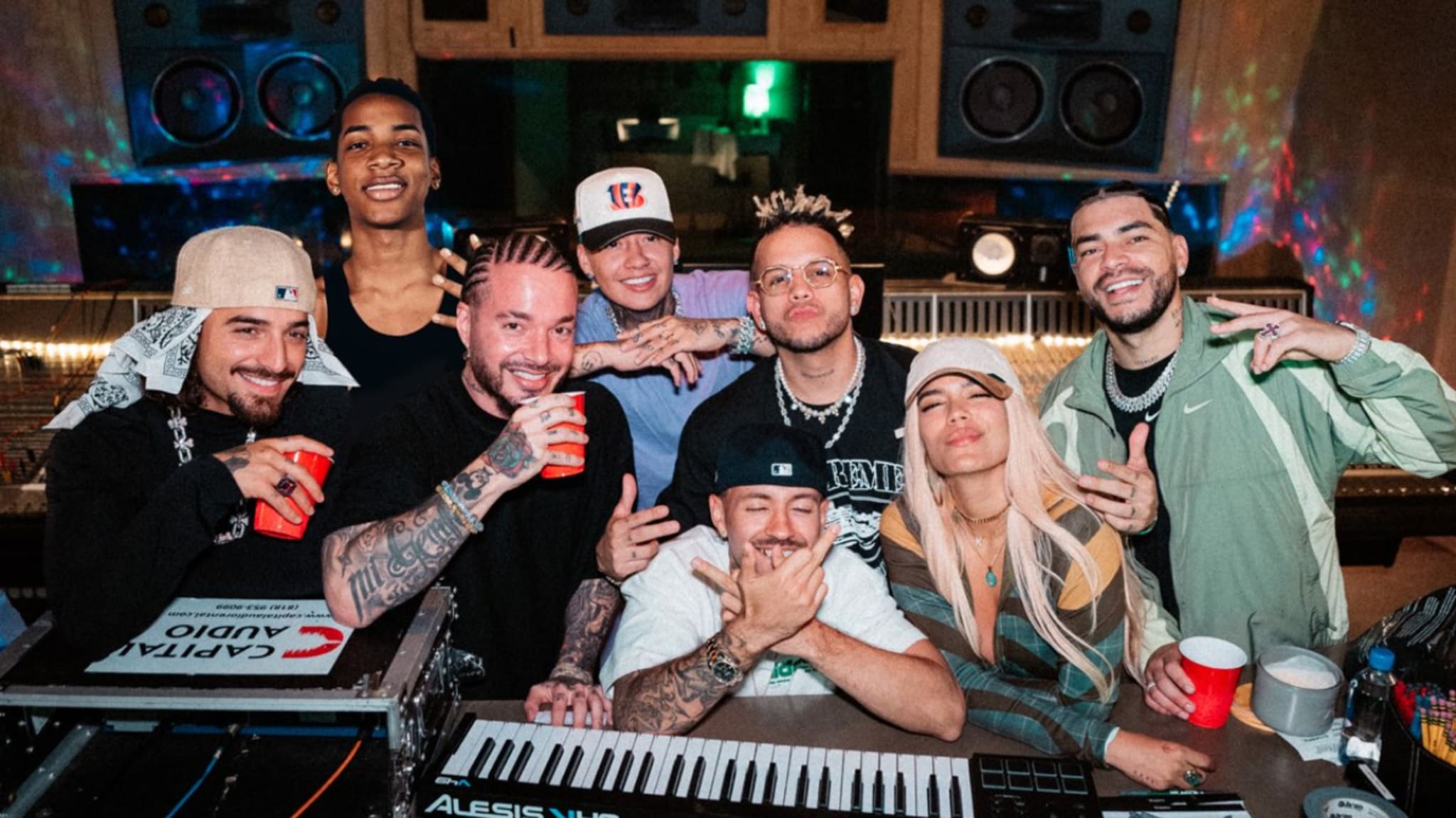 A group of people in a recording studio, including J Balvin and Karol G, smiling and posing with musical equipment.