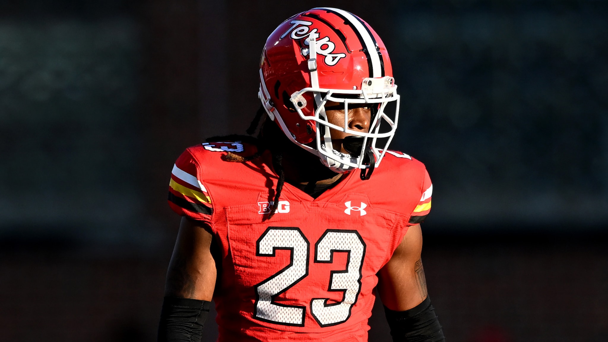 A football player in a red uniform and helmet with "Terps" logo, wearing number 23, stands on the field.